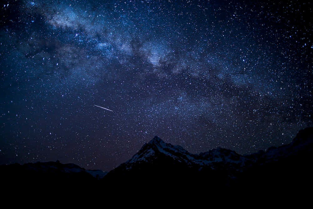 湖面之上繁星滿天 壁紙 — 令人屏息的夜空，滿天繁星和銀河拱起在積雪的山峰之上，一顆流星劃過天際。