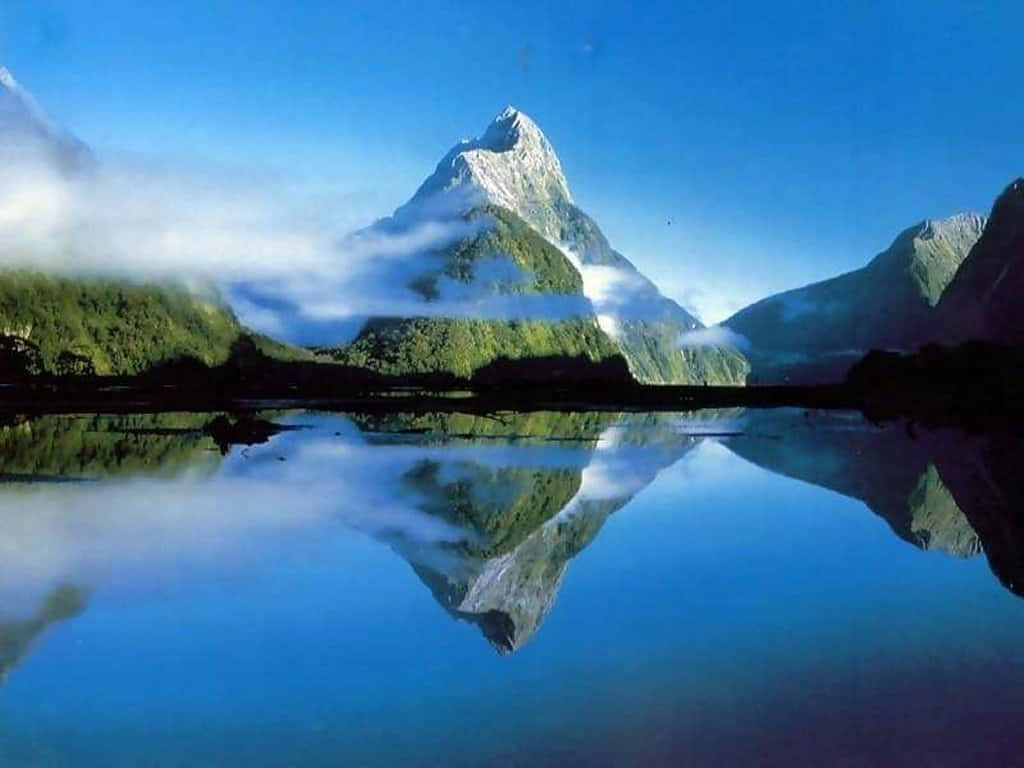 湖面倒影的美麗山景 壁紙 — 雄偉的雪山峰頂在清澈藍天下，透過薄霧窺視著如鏡的湖面，完美倒映其中。