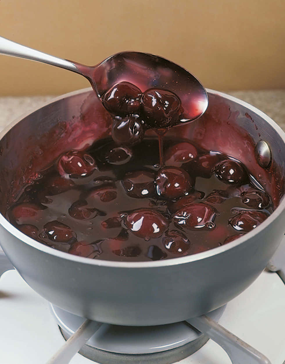 Black Cherry 桌布 壁紙 — 湯匙從爐上的平底鍋中舀起光澤的深色櫻桃蜜餞，展現出濃郁的糖漿質感。