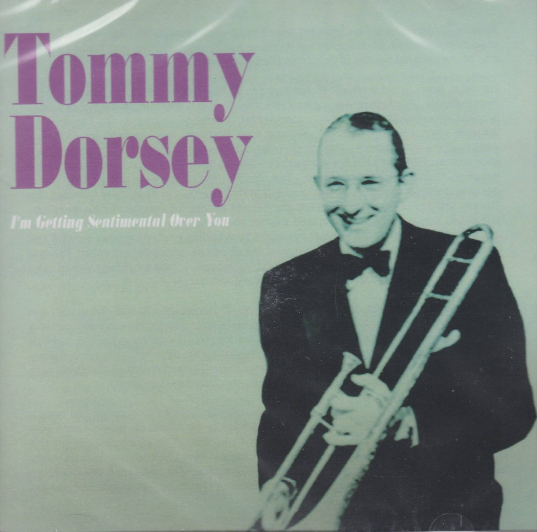 湯米·多西演奏小號黑白照片 壁紙 — 一張復古爵士專輯封面，Tommy Dorsey 在淺綠色背景前溫暖微笑，手持長號。