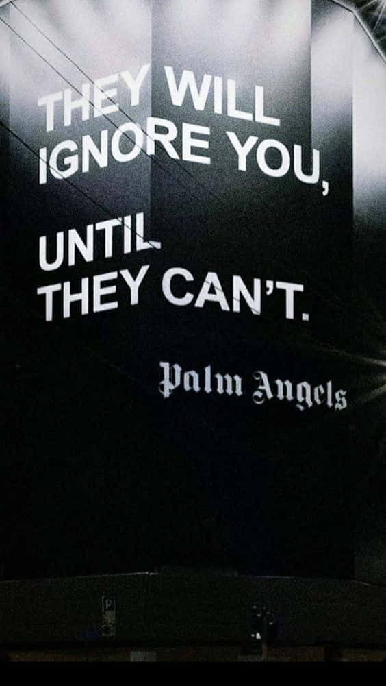 深色牆上以粗體白色文字寫著「THEY WILL IGNORE YOU UNTIL THEY CAN'T」及下方「Palm Angels」。