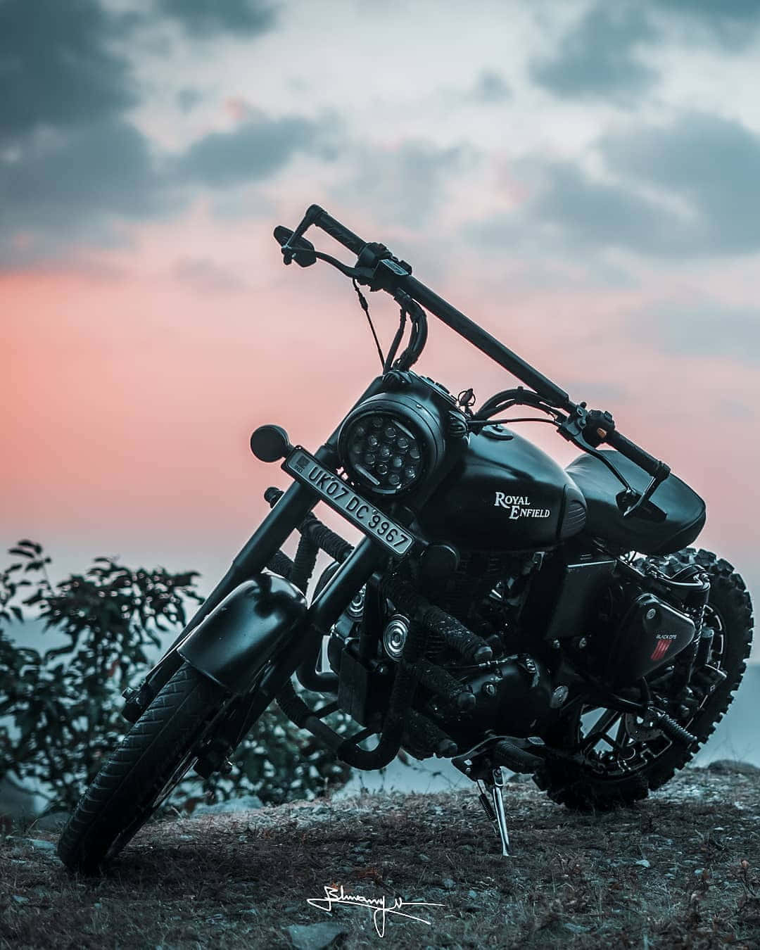 日落時分，黑色 Royal Enfield 電單車停泊喺山丘上。