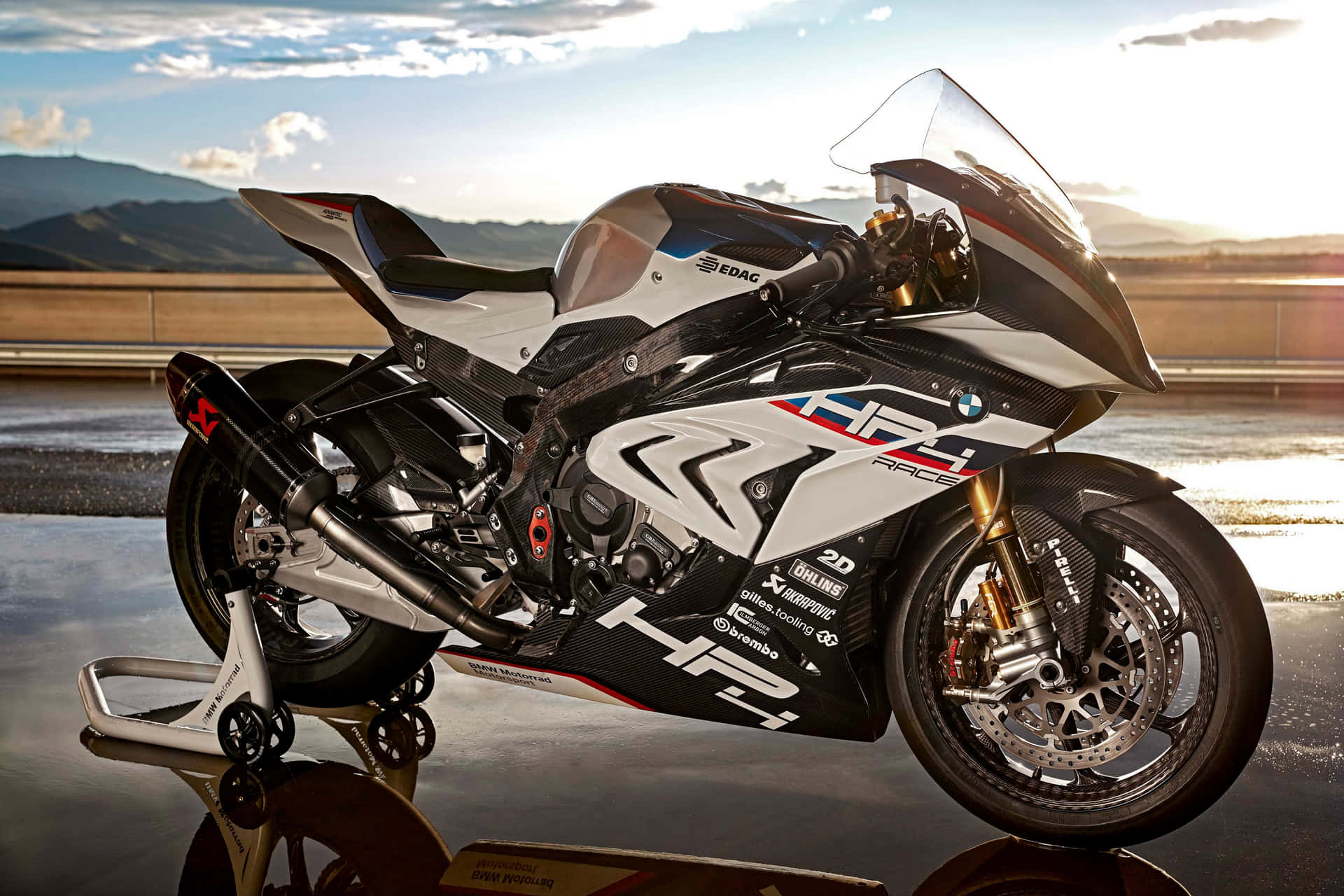 BMW HP4 Race電單車在金色日落時分的濕路上，山景為背景。