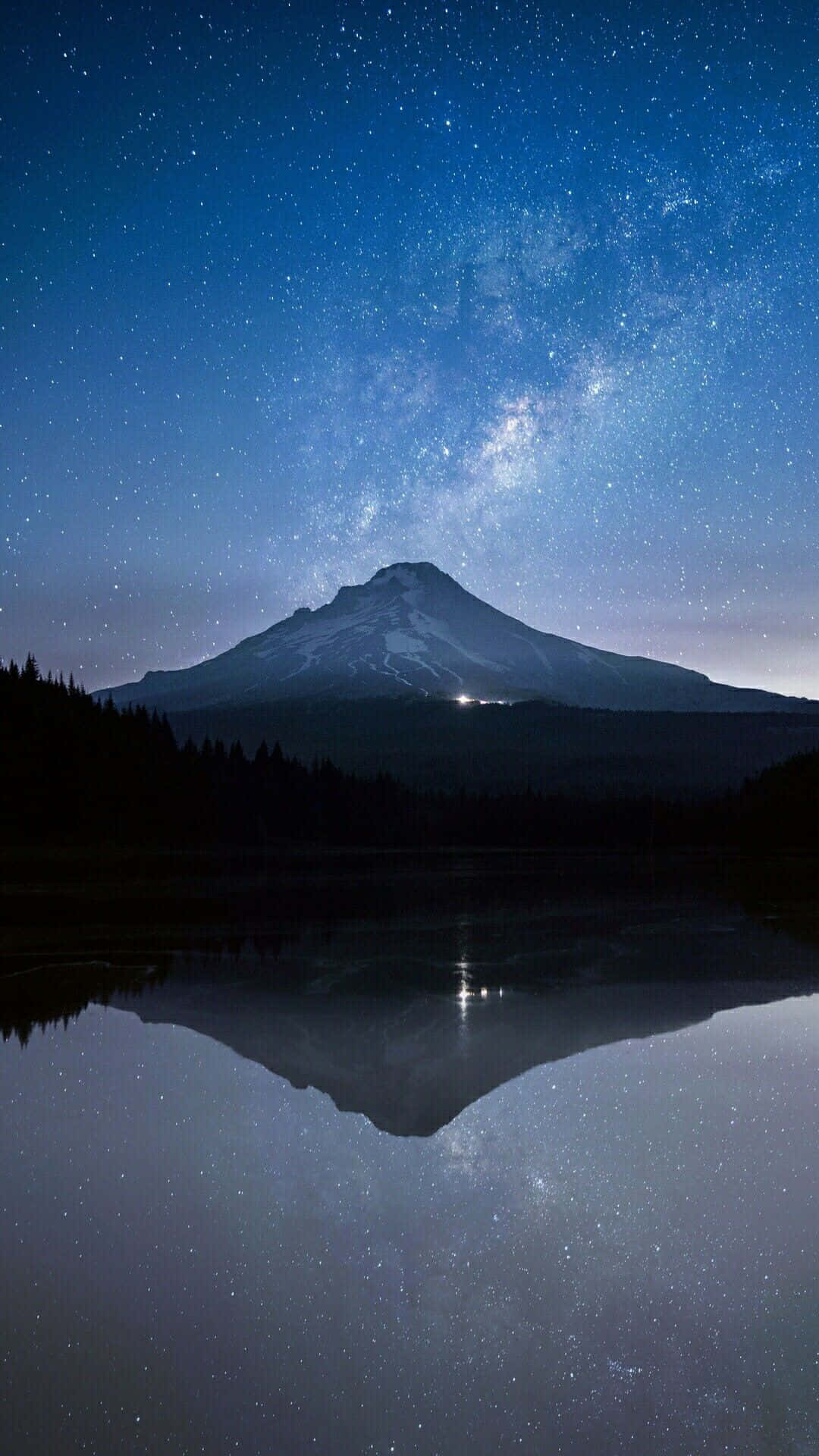 山峰和星空在夜晚平靜的湖面上形成倒影。