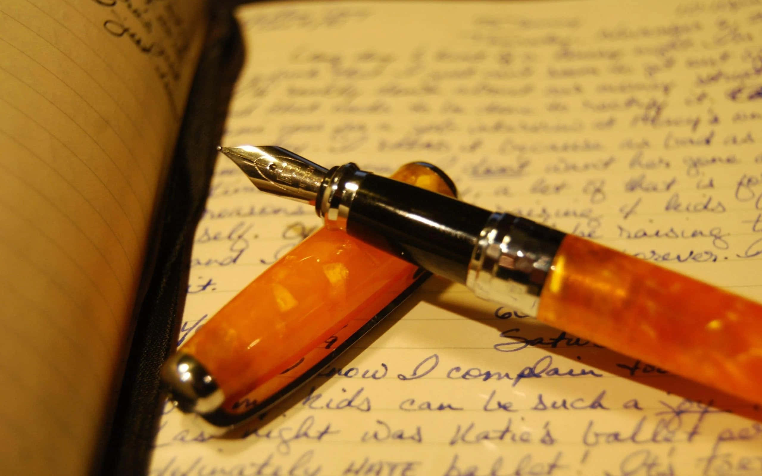 準備好，拿起筆吧！ 壁紙 — 橙色半透明鋼筆特寫，擱在帶橫線的筆記本上手寫筆記上。