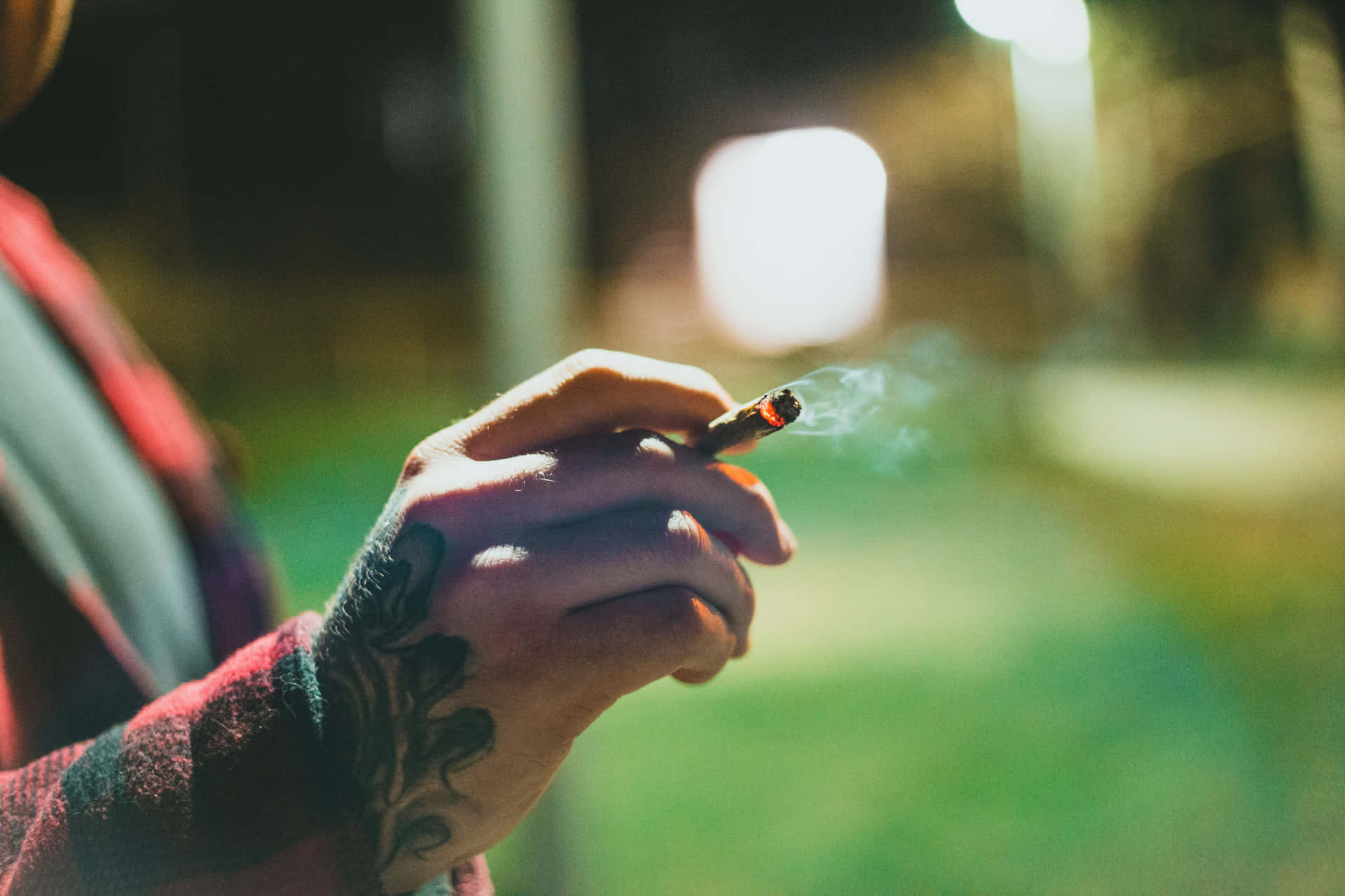 帶有紋身的手在夜間拿著點燃的香煙，背景模糊的燈光