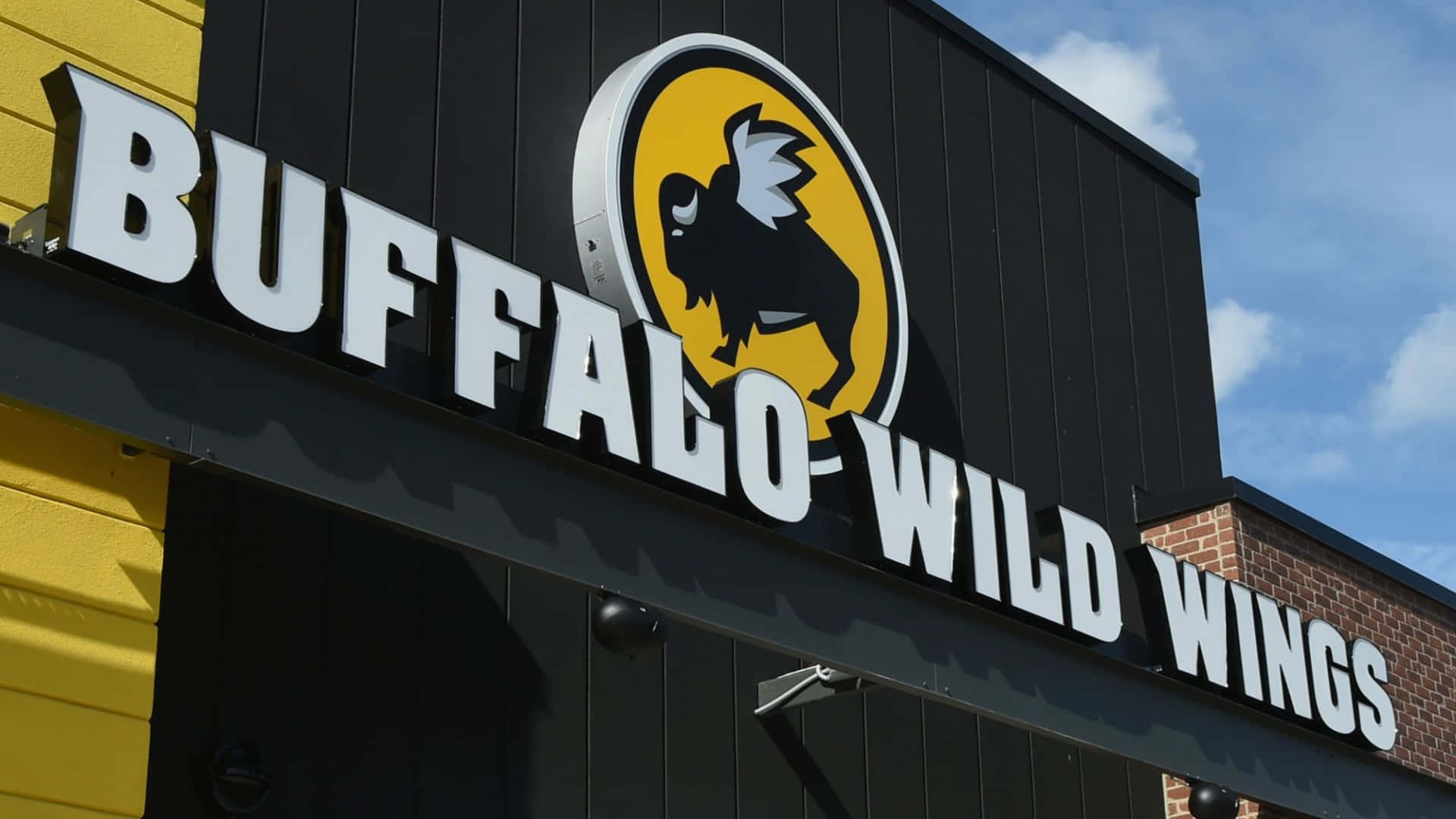 藍天下黑黃建築物上的 Buffalo Wild Wings 餐廳招牌。