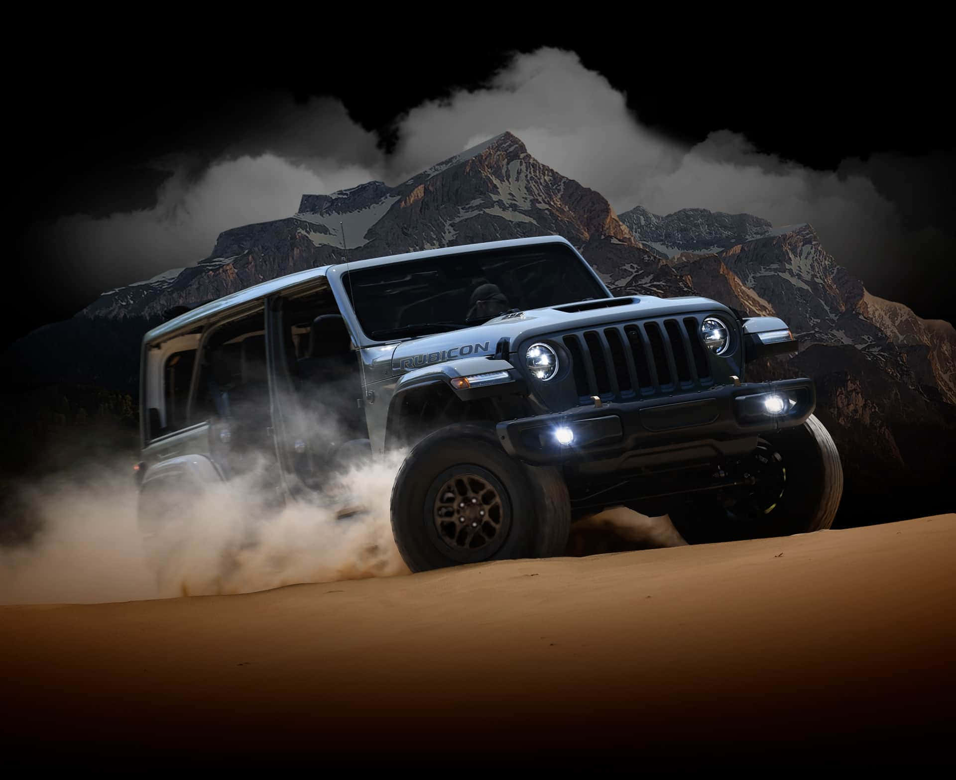 銀色Jeep Rubicon夜間在沙漠沙地上行駛，背景有山脈。