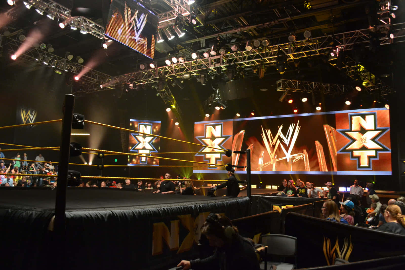 準備好摔角比賽 壁紙 — WWE NXT 摔角擂台在明亮的舞台燈光下，前景有粉絲，上方有大型品牌屏幕。