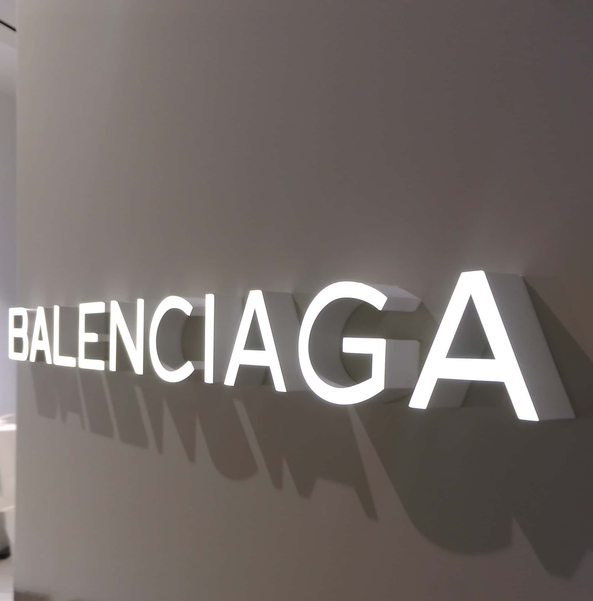 灰色牆壁上發光的 Balenciaga 標誌投下陰影。