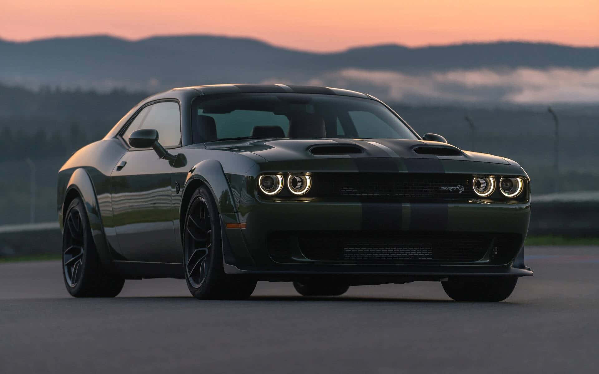 深綠色Dodge Challenger SRT Hellcat在日落時分的賽道上，背後有霧氣繚繞的山脈。