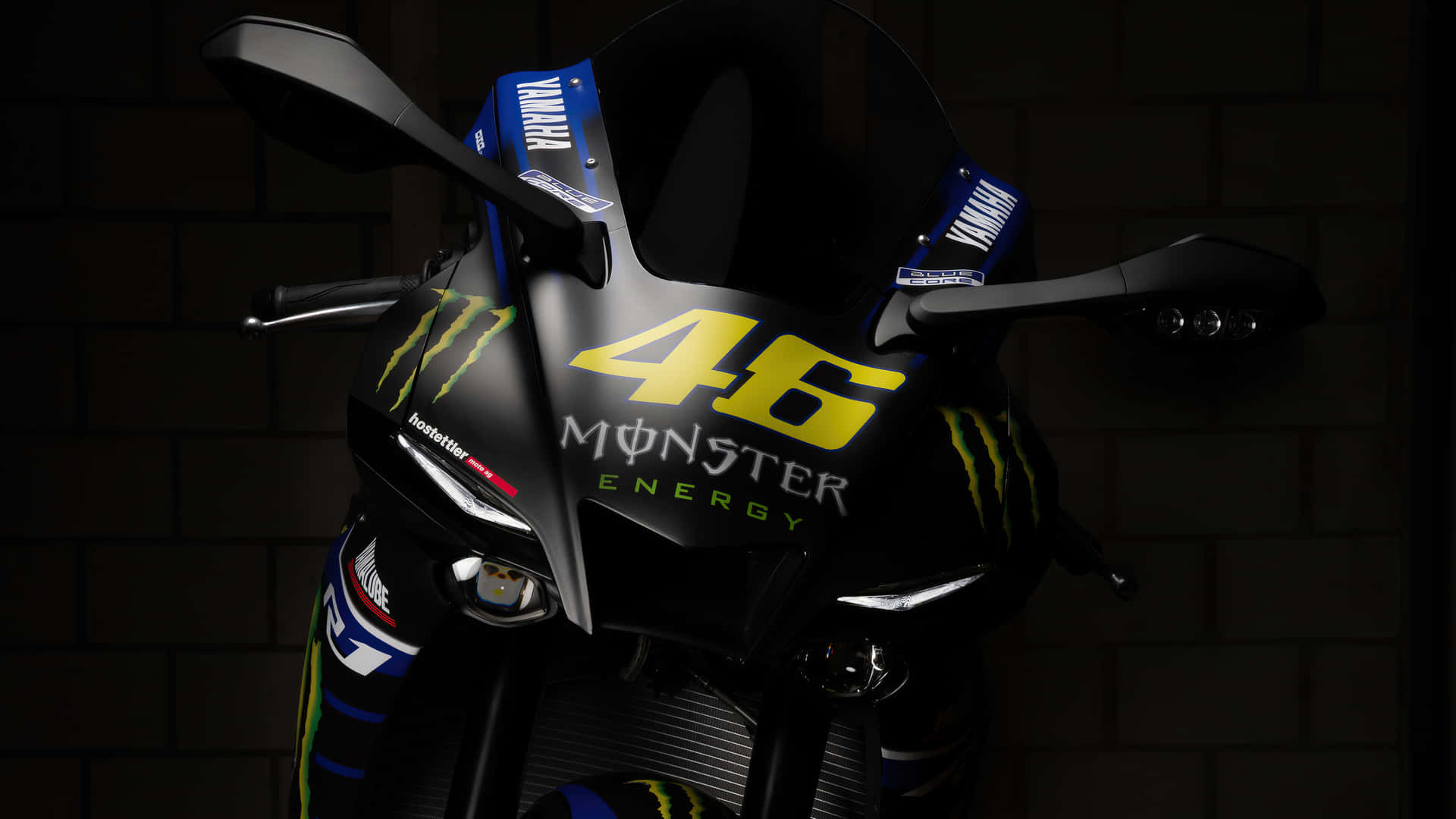 黑色Yamaha賽車電單車，帶有黃色46 Monster Energy標誌，背景為磚牆。