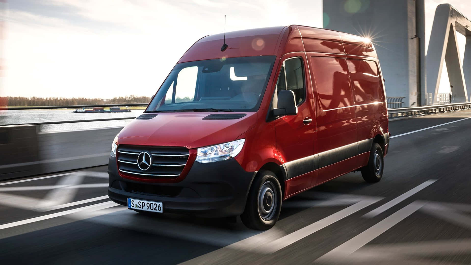 紅色 Mercedes-Benz Sprinter 客貨車在日落時分行駛在橋上。