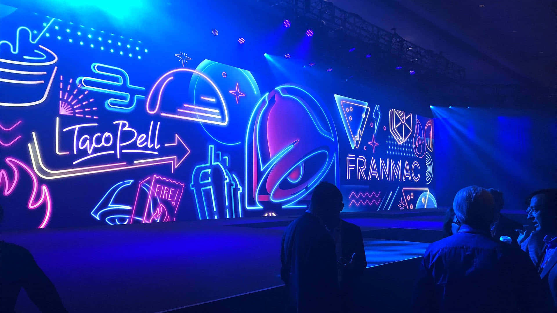 觀眾觀看一個霓虹燈照亮、帶有 Taco Bell 和 Franmao 標誌的舞台。