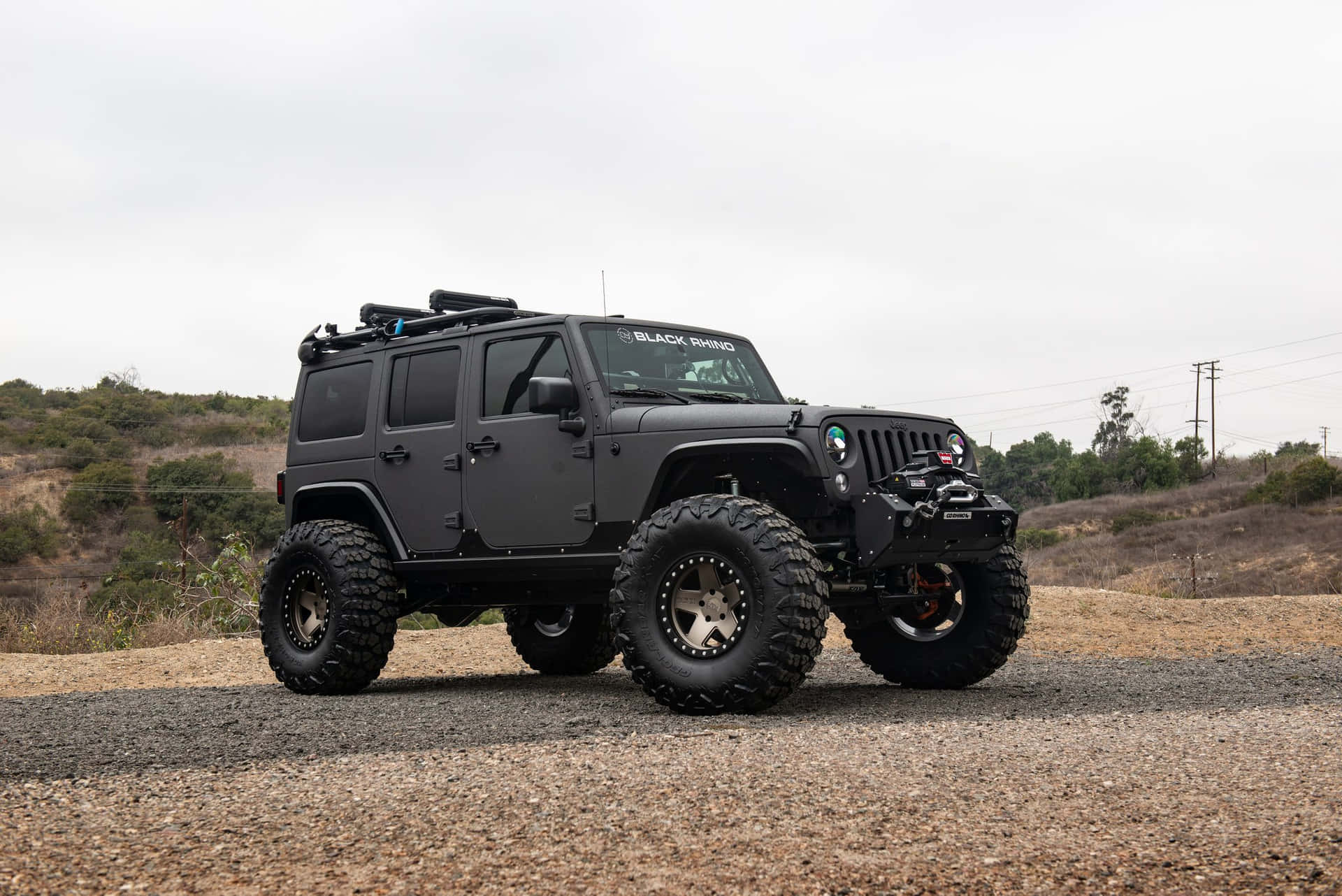 黑色升高Jeep Wrangler停泊在碎石路上，背景有丘陵地形。
