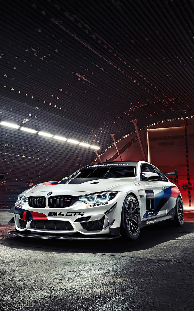在光線昏暗的車庫中，一輛帶有藍紅塗裝的白色BMW M4 GT4賽車。