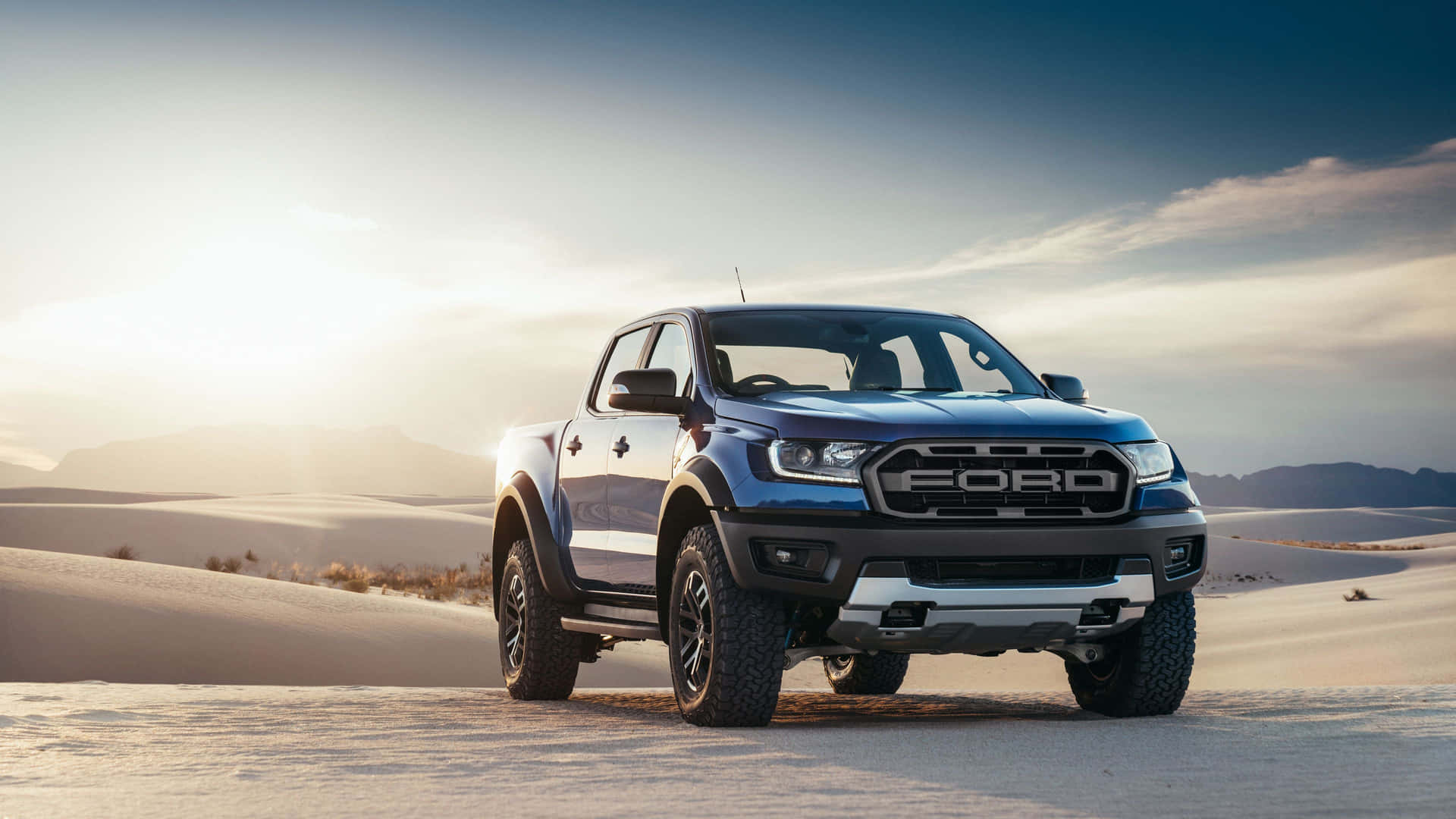 日落時分停在沙漠沙丘上的藍色福特 Ranger Raptor。