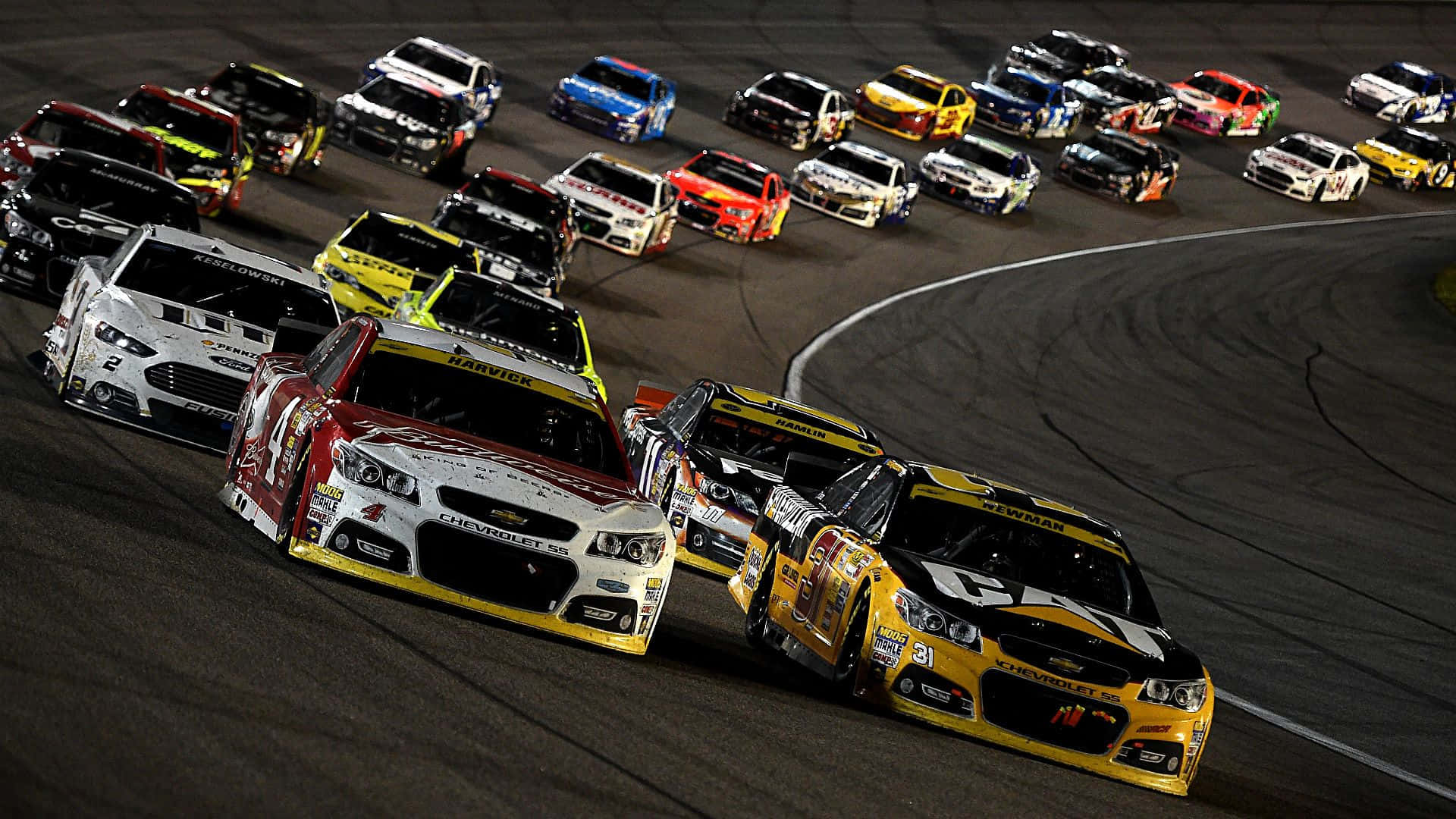 NASCAR賽車在明亮燈光下於夜間賽道上飛馳。