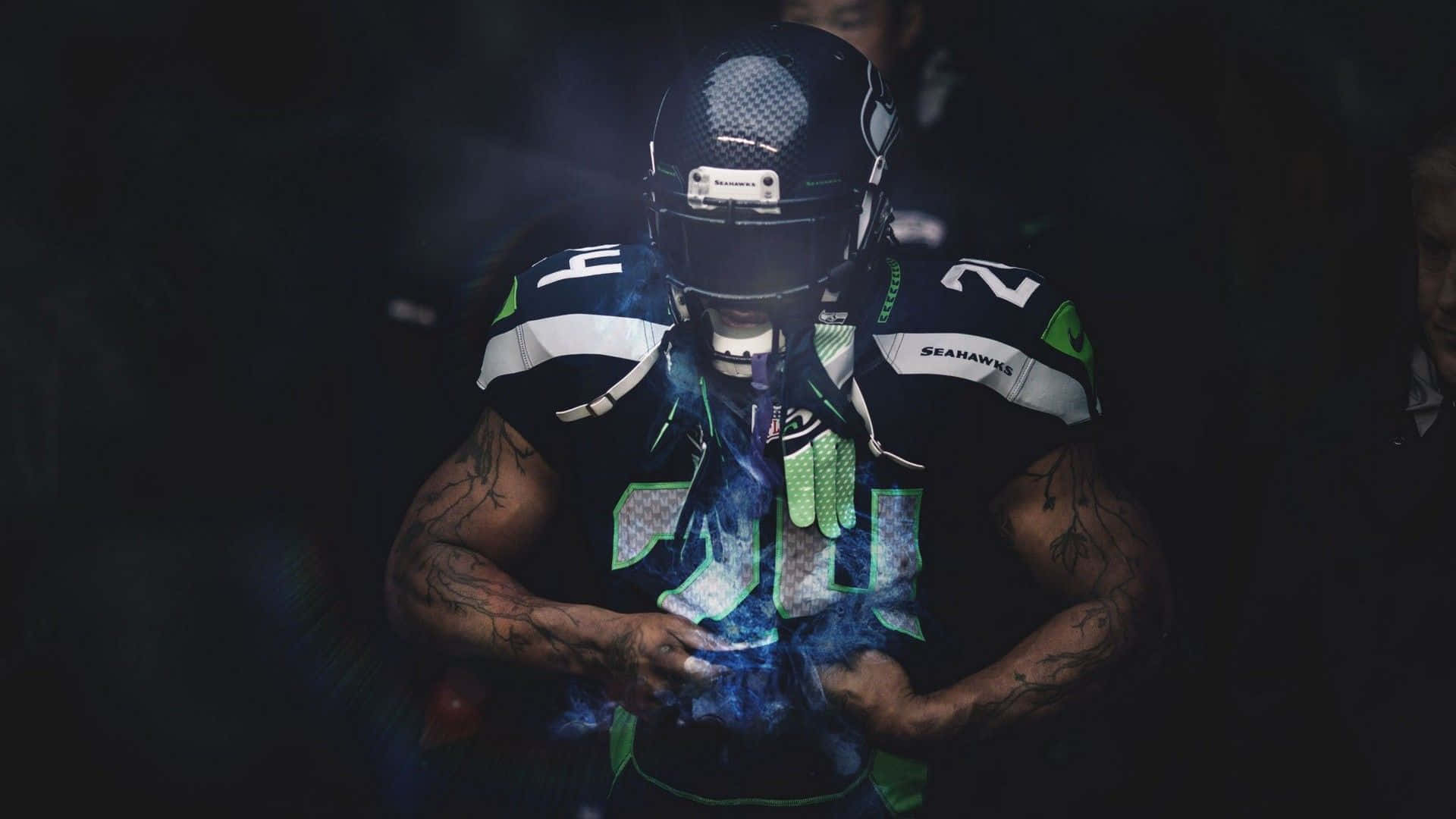 準備迎接下一場大賽，高清NFL壁紙 壁紙 — 一名西雅圖海鷹隊美式足球員身穿深色裝備，站在煙霧繚繞的陰影中，藍色發光能量在他雙手周圍旋轉。
