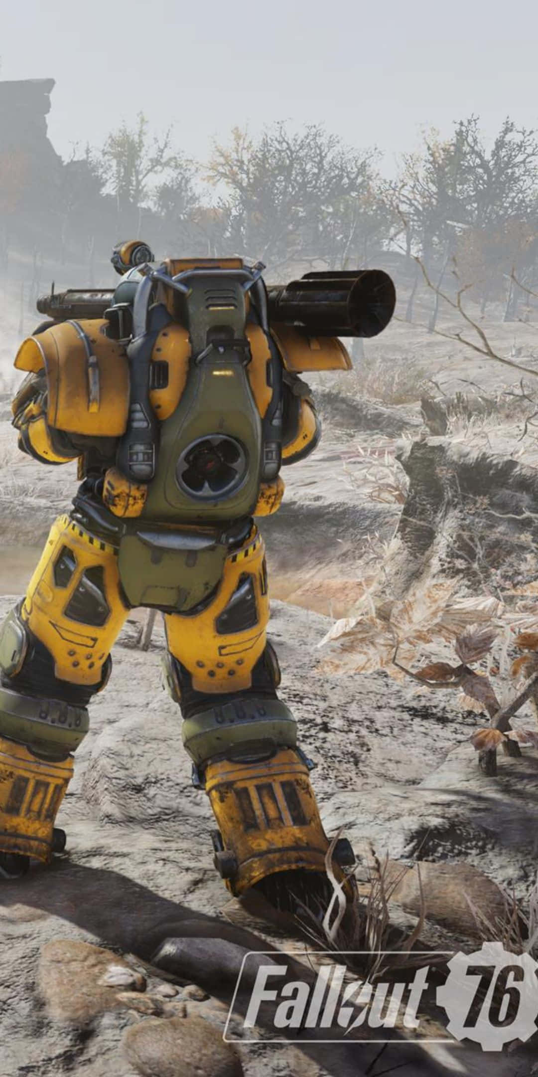 準備迎接你的下一次冒險，搭配 Pixel 3 與 Fallout 76！ 壁紙 — 一套黃綠色的動力裝甲套裝，站在一片荒涼、多岩石的荒原上，有光禿禿的樹木，天空朦朧。
