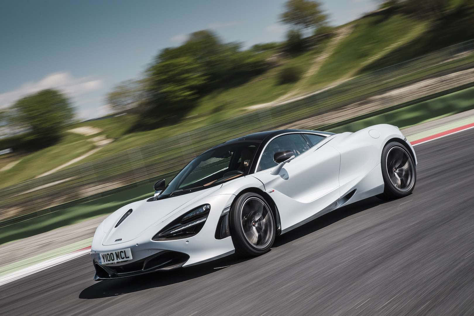 白色McLaren 720S在賽道上飛馳，背景有綠色山丘和藍天。
