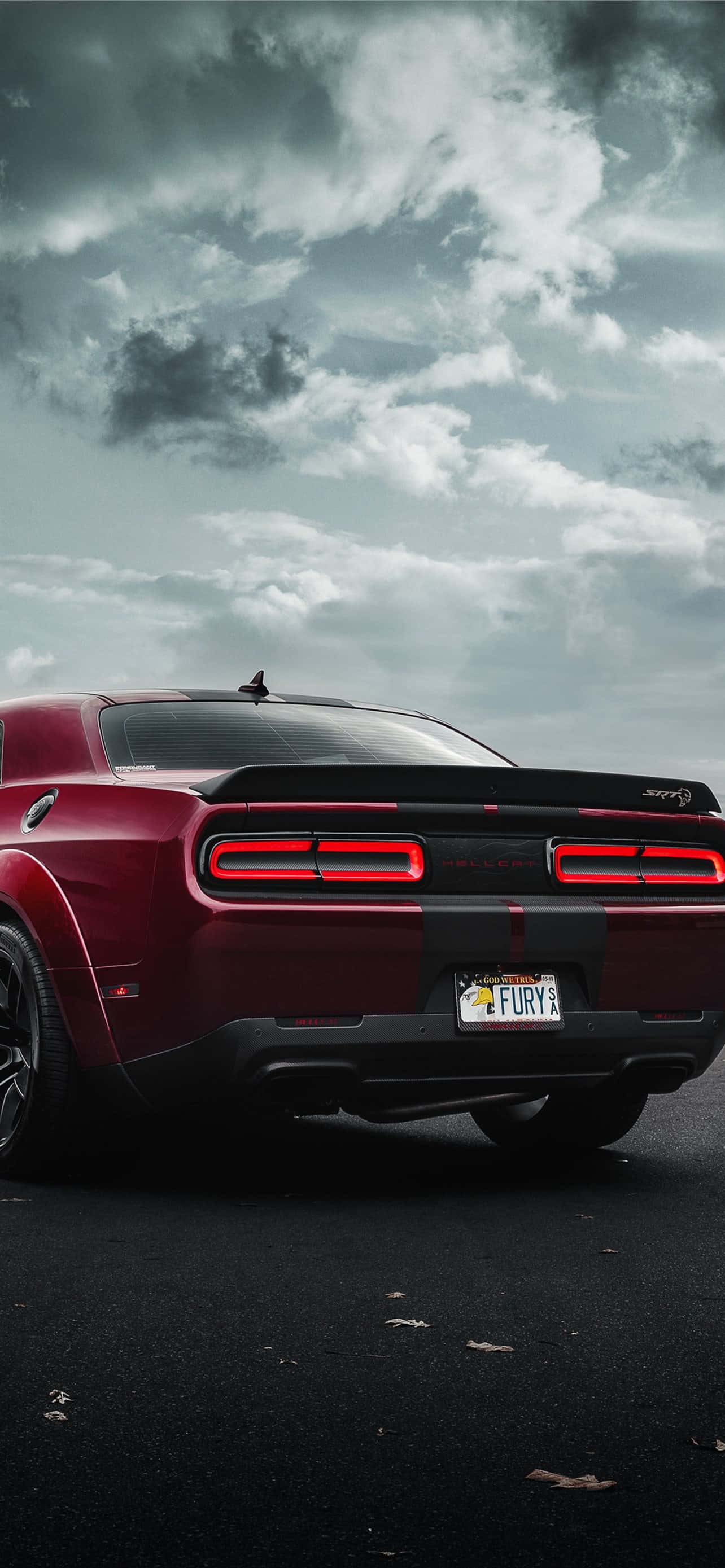 準備迎接速度：選配iPhone Hellcat處理器 壁紙 — 一架紅色Dodge Challenger Hellcat，亮著尾燈，停泊在戲劇性的多雲天空下濕漉漉的瀝青路上。