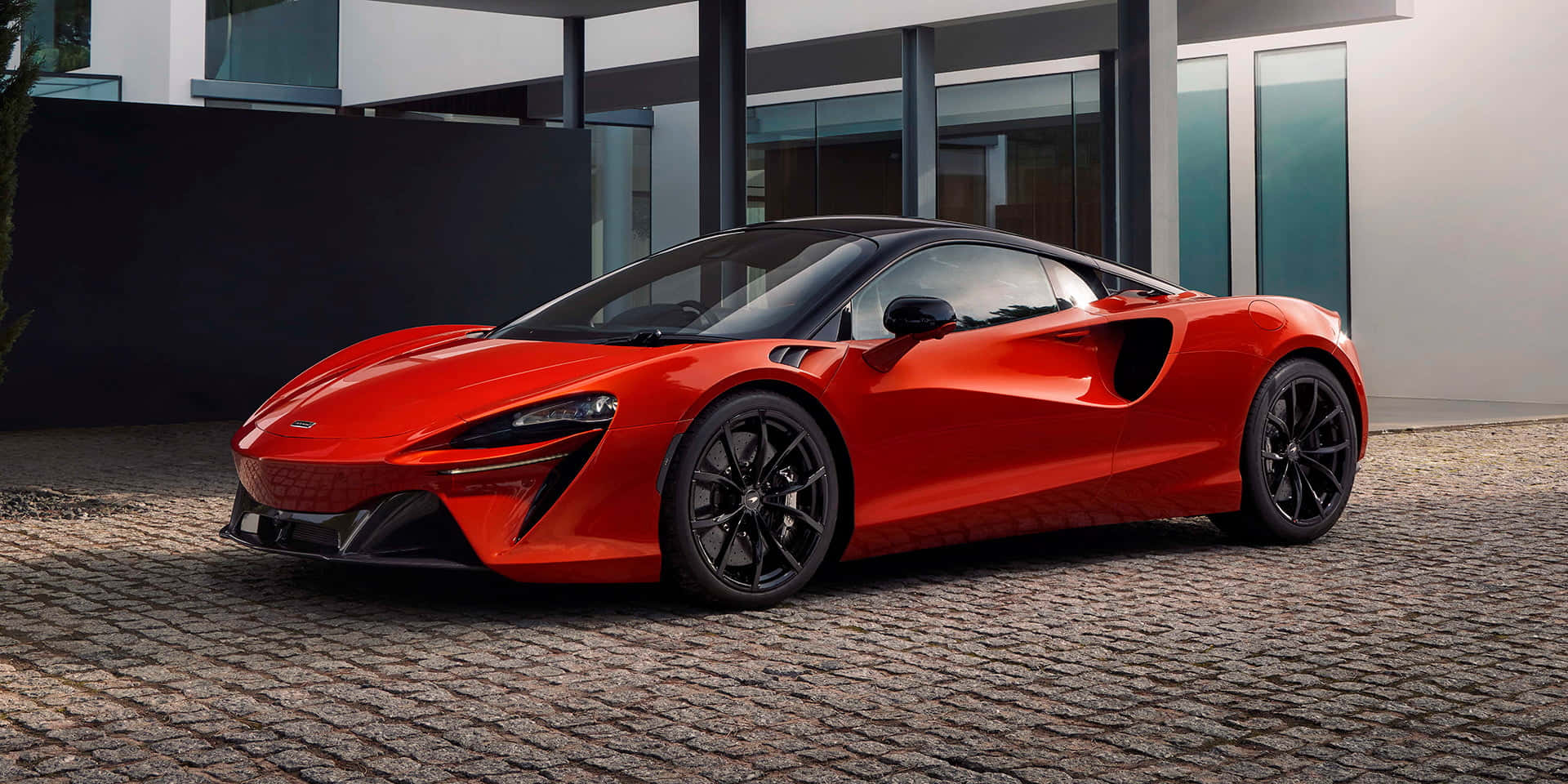 紅色McLaren跑車停在現代玻璃屋前的鵝卵石上。