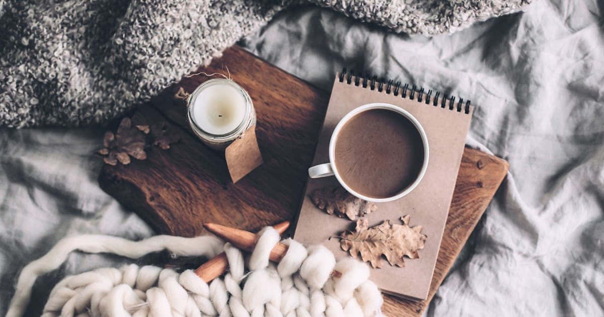 舒適的秋日早晨佈置，咖啡杯、筆記本、蠟燭和羊毛毯子放在床上。 — 冬季 壁紙