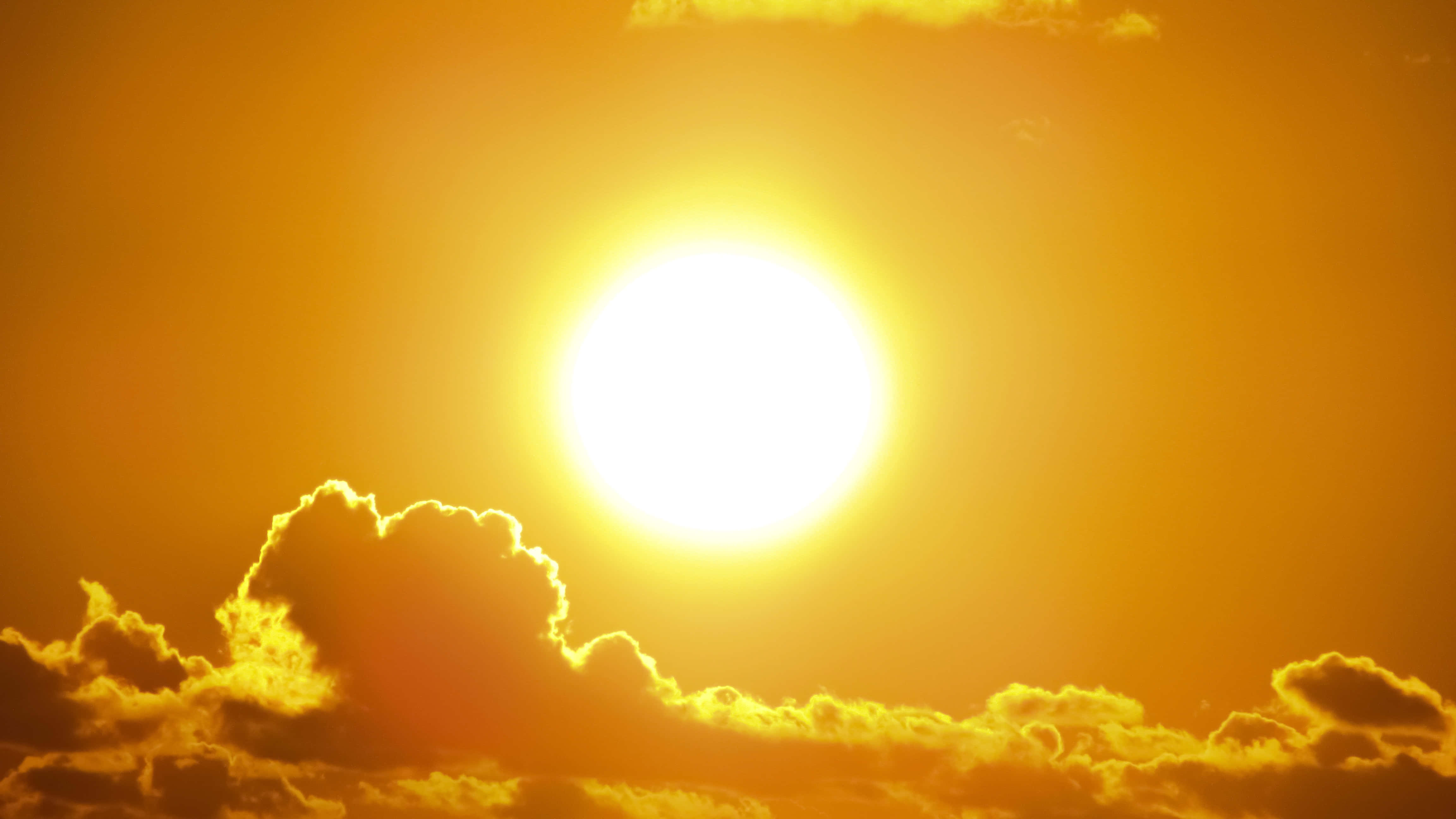 溫暖晴日，萬事皆宜 壁紙 — 一顆燦爛的太陽在金色橙色的天空中燃燒，將熾熱的光芒投射在下方戲劇性的雲層上。