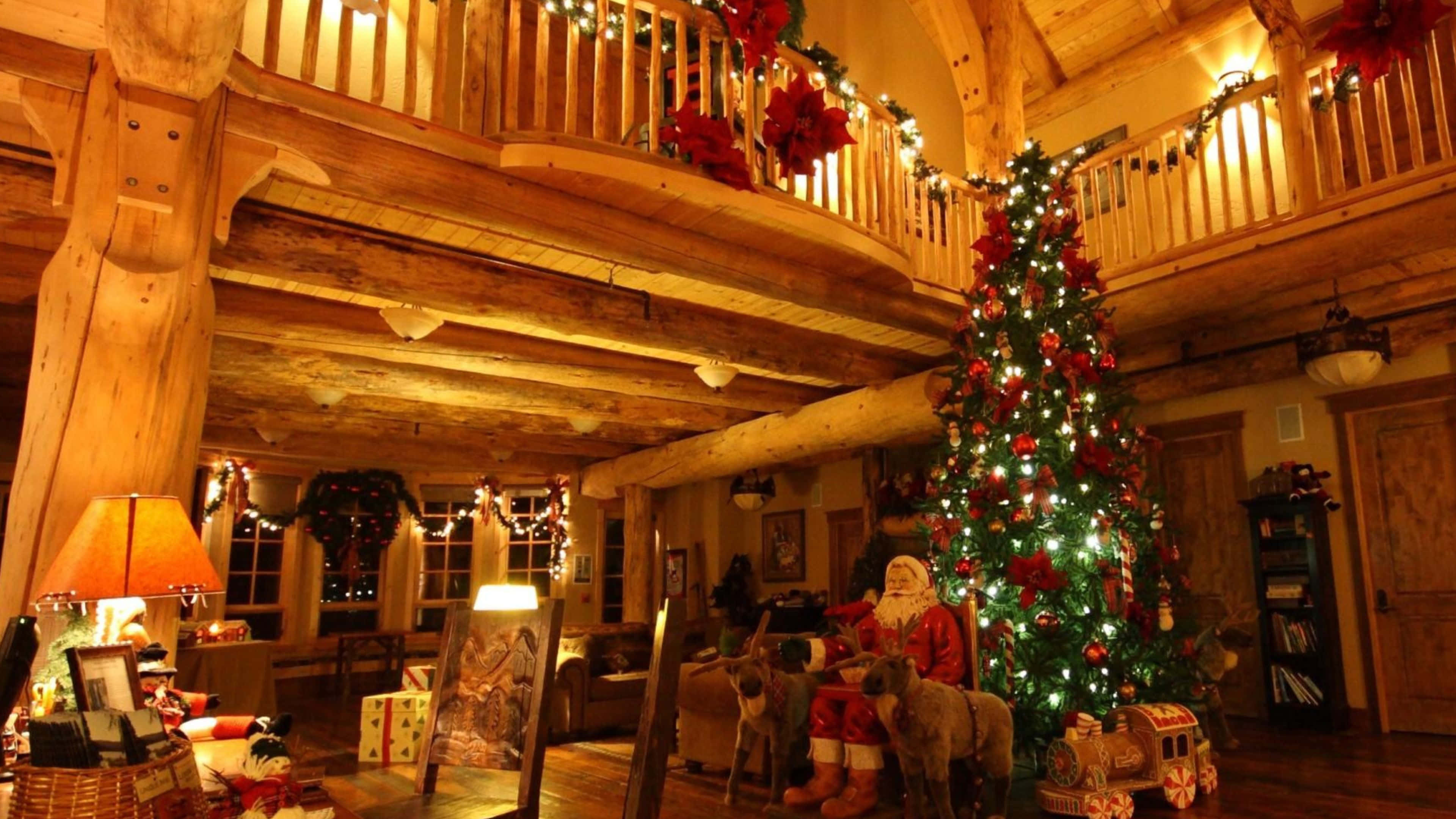 Rustic Christmas 桌布 壁紙 — 溫暖照明的鄉村木屋內部，裝飾著發光的聖誕樹和節日花環，充滿聖誕氣氛。