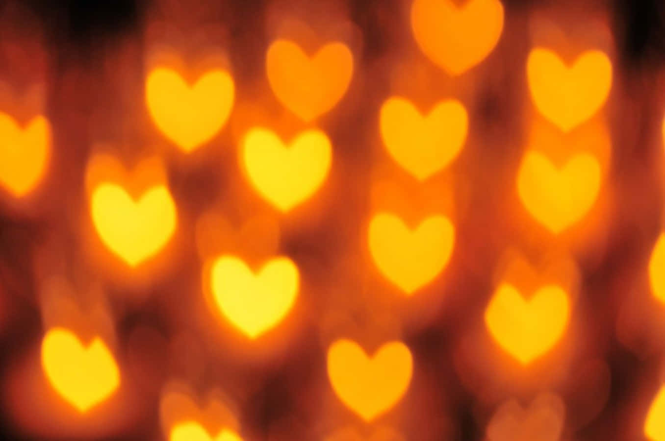 Orange Heart 桌布 壁紙 — 溫暖的散景效果，發光的橙色心形燈光在黑暗背景下柔和模糊。
