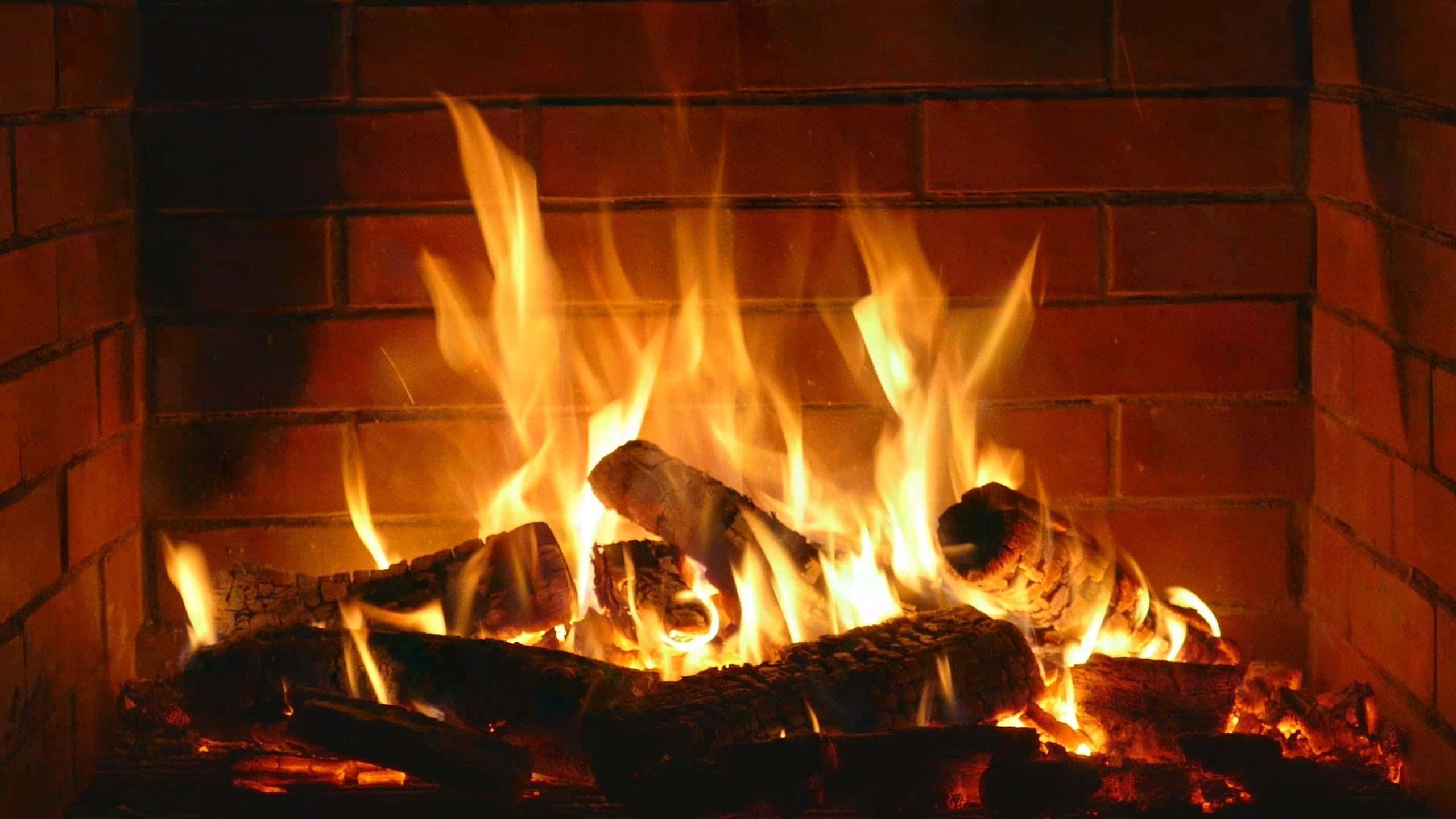 Cozy Fire 桌布 壁紙 — 溫暖的金色火焰從鄉村磚砌壁爐中噼啪作響的木柴上躍起，在周圍的磚塊上投下柔和的光線。