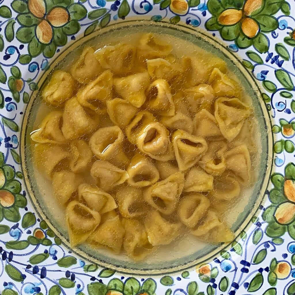 溫暖義大利美食——布羅多湯通心粉 壁紙 — 從上方俯瞰，玻璃碗中的高湯義大利餃放在彩色花卉盤上。