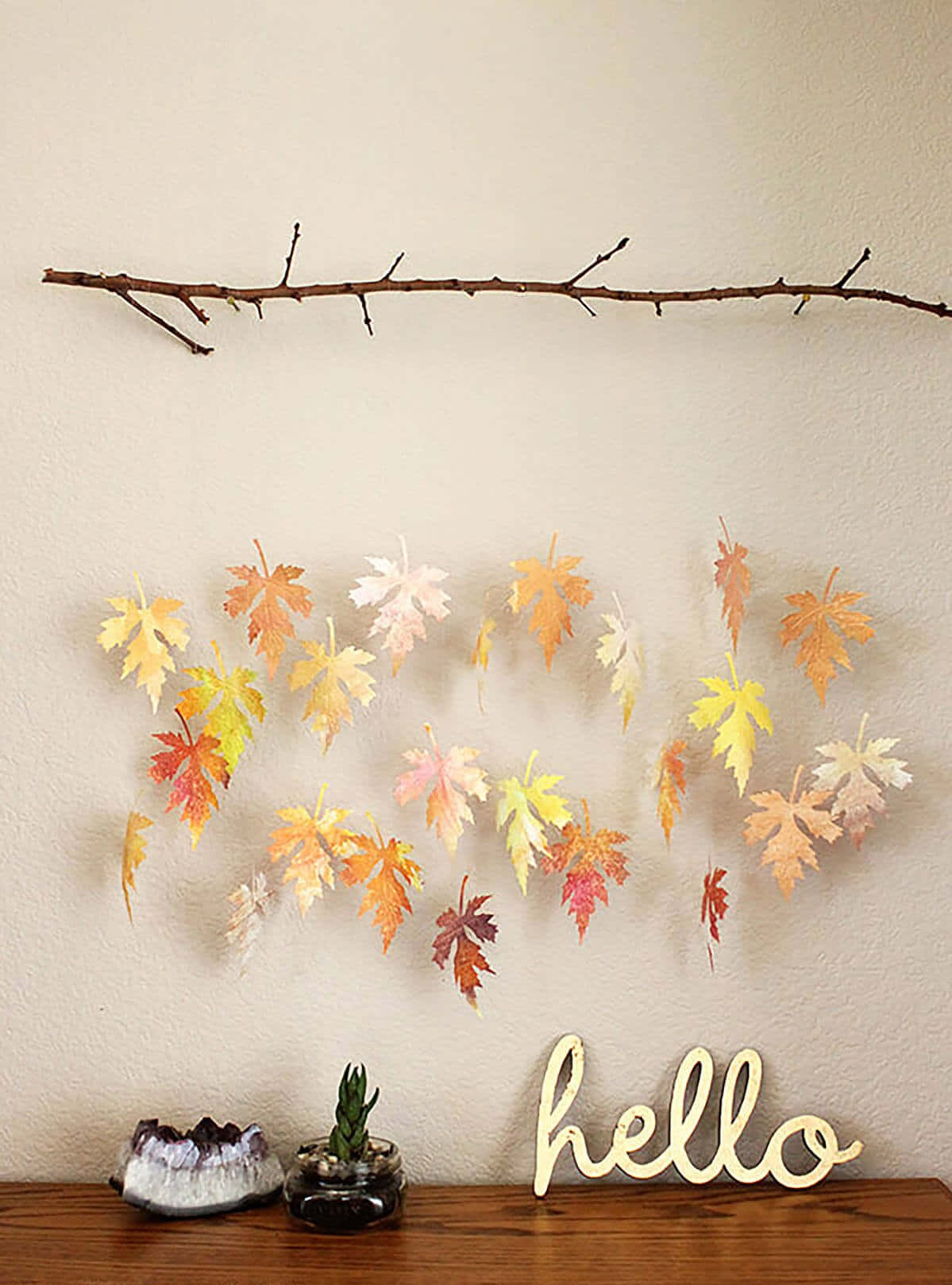 Fall Crafts 桌布 壁紙 — 溫暖色調的秋葉從光禿的樹枝上垂下來，映襯著米色牆壁，下方木架上放著 hello 標誌和小植物。
