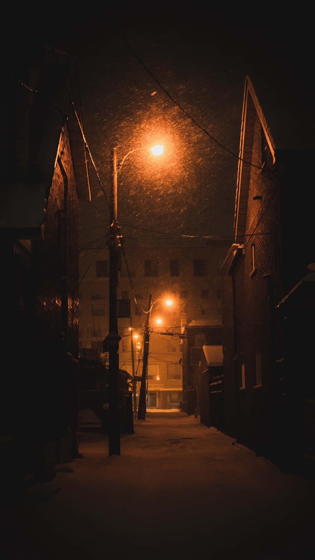 夜晚被溫暖路燈照亮的雪中城市小巷。