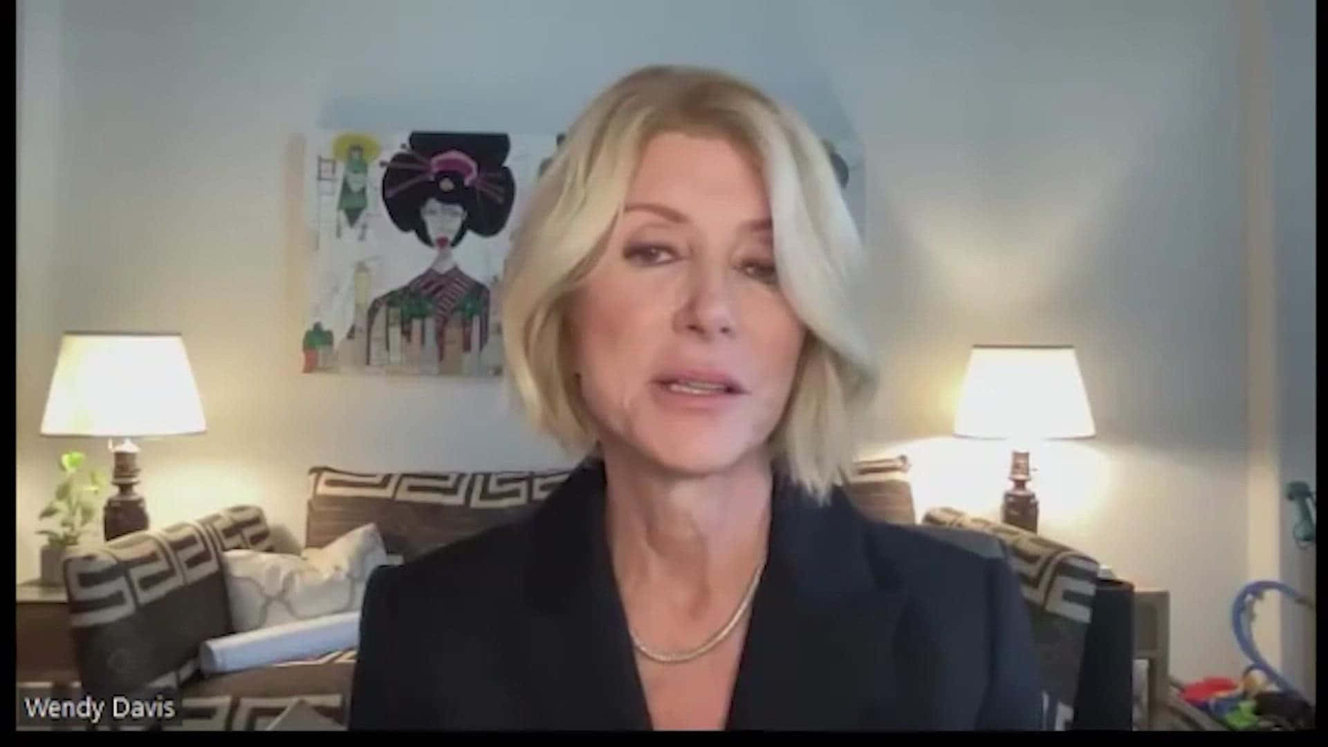 一位穿著深色西裝外套的女性坐在光線充足的客廳中，周圍有圖案家具和藝術品。