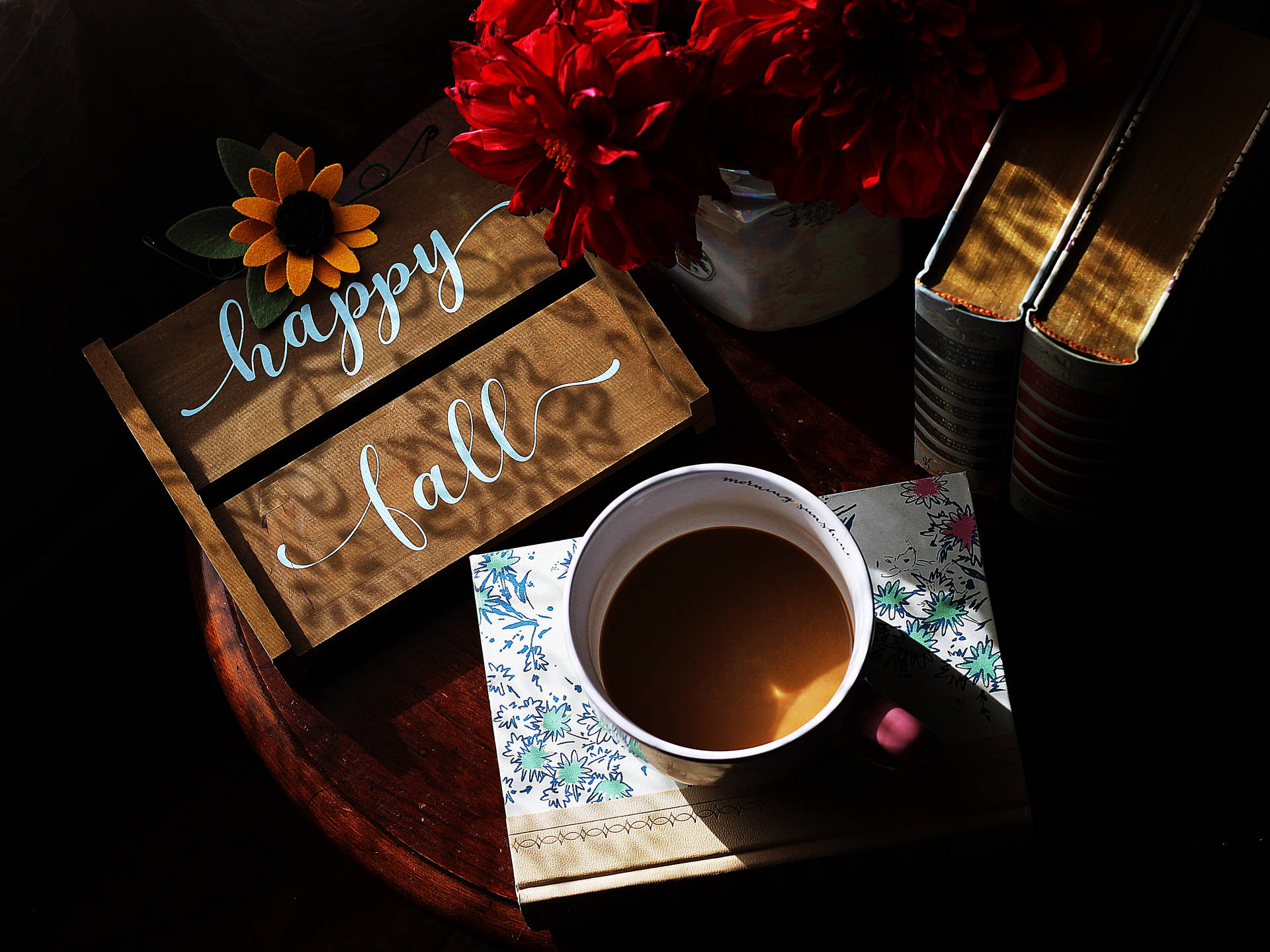 舒適的秋日桌面，有咖啡、書籍、紅花和一個happy fall標誌。
