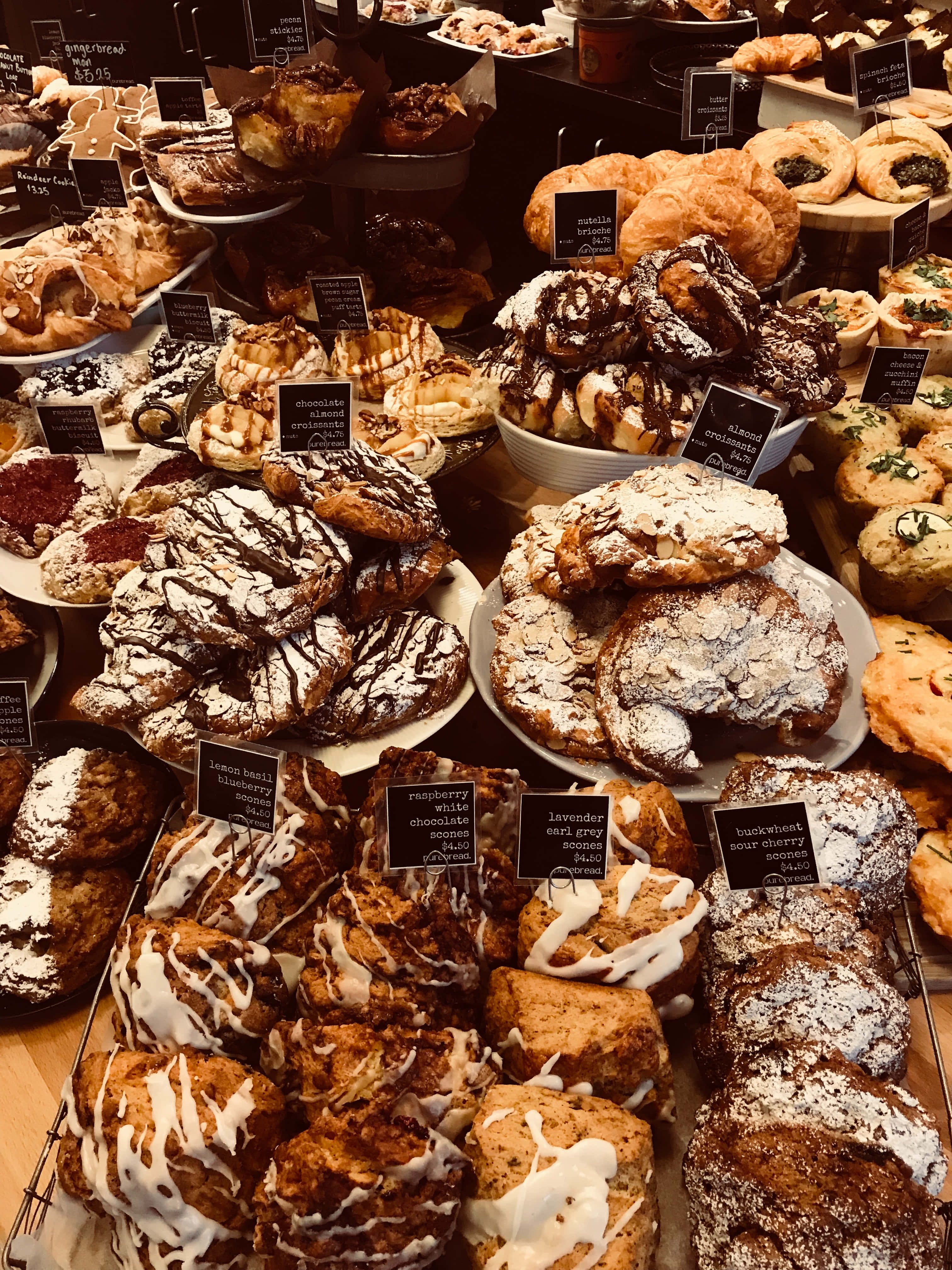 溫馨麵包店裡的新鮮烘焙美味 壁紙 — 一個豪華的麵包店展示櫃，堆滿了淋上朱古力和糖霜的各式糕點。