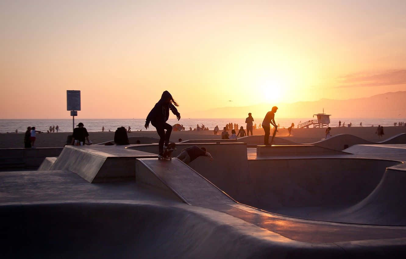 skateboarding 桌布 壁紙 — 滑板手在海邊滑板公園的混凝土坡道上滑行，夕陽在海洋上空落下，投射出溫暖的金色光芒。