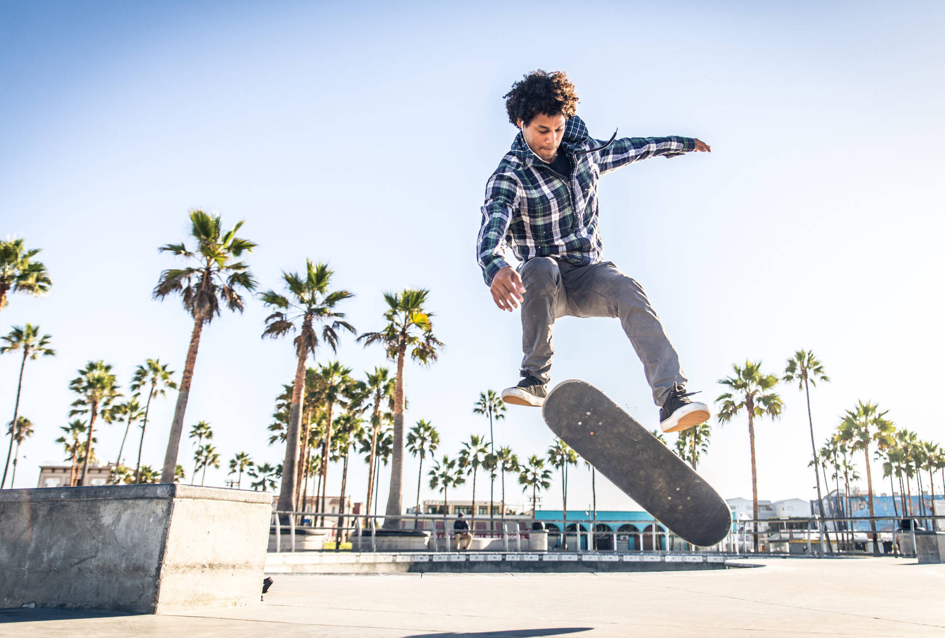 滑板手空中執行 Nollie FS Pop Shove-it 壁紙 — 一名年輕滑板手在半空中以棕櫚樹和清澈藍天為背景表演技巧。