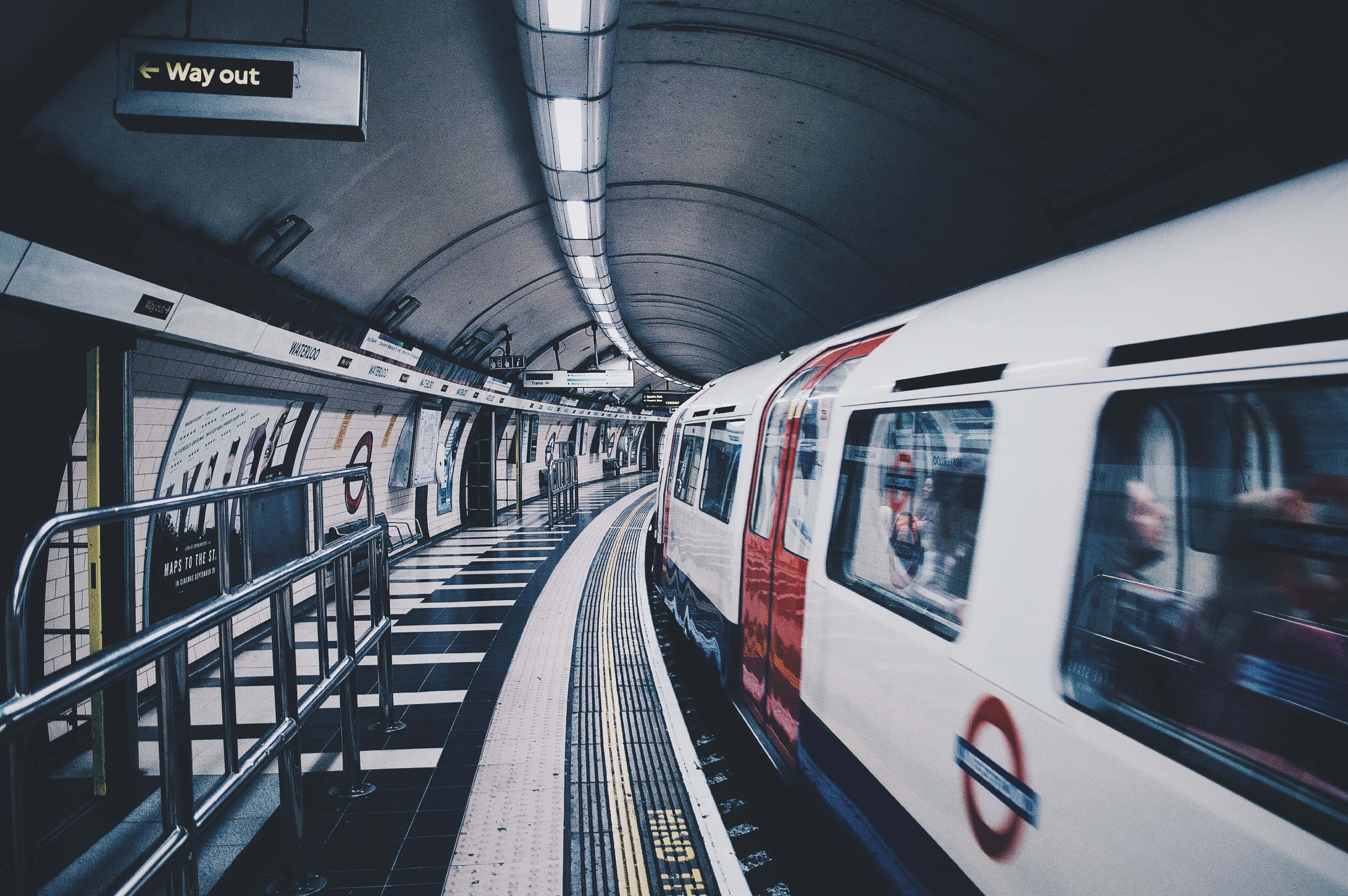 滑鐵盧車站列車 壁紙 — 一列倫敦地鐵列車高速駛過一個彎曲的月台，月台有瓷磚牆壁和頭頂上的「Way out」標誌。