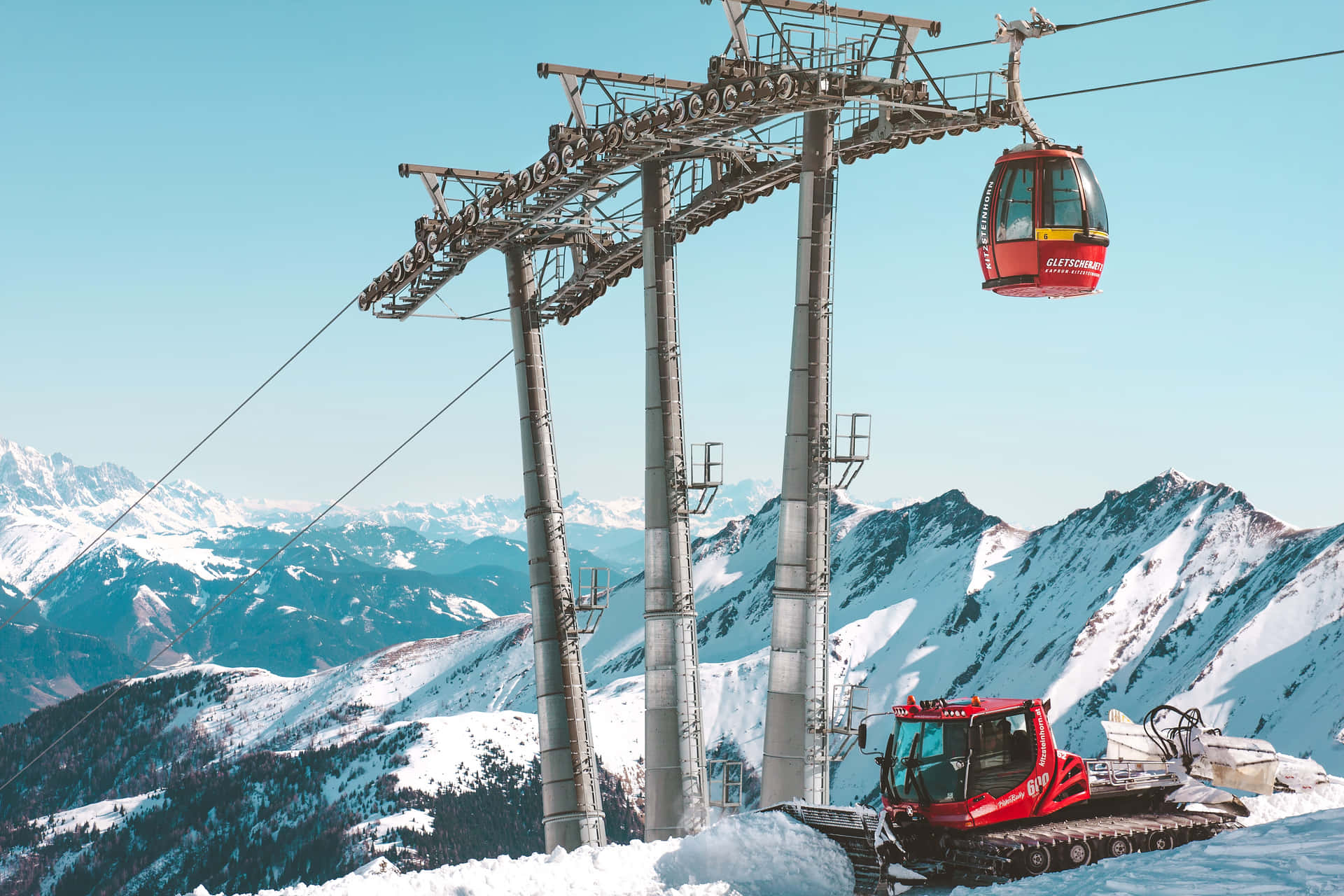 晴朗藍天下，白雪覆蓋的山坡上的紅色纜車和雪地車。