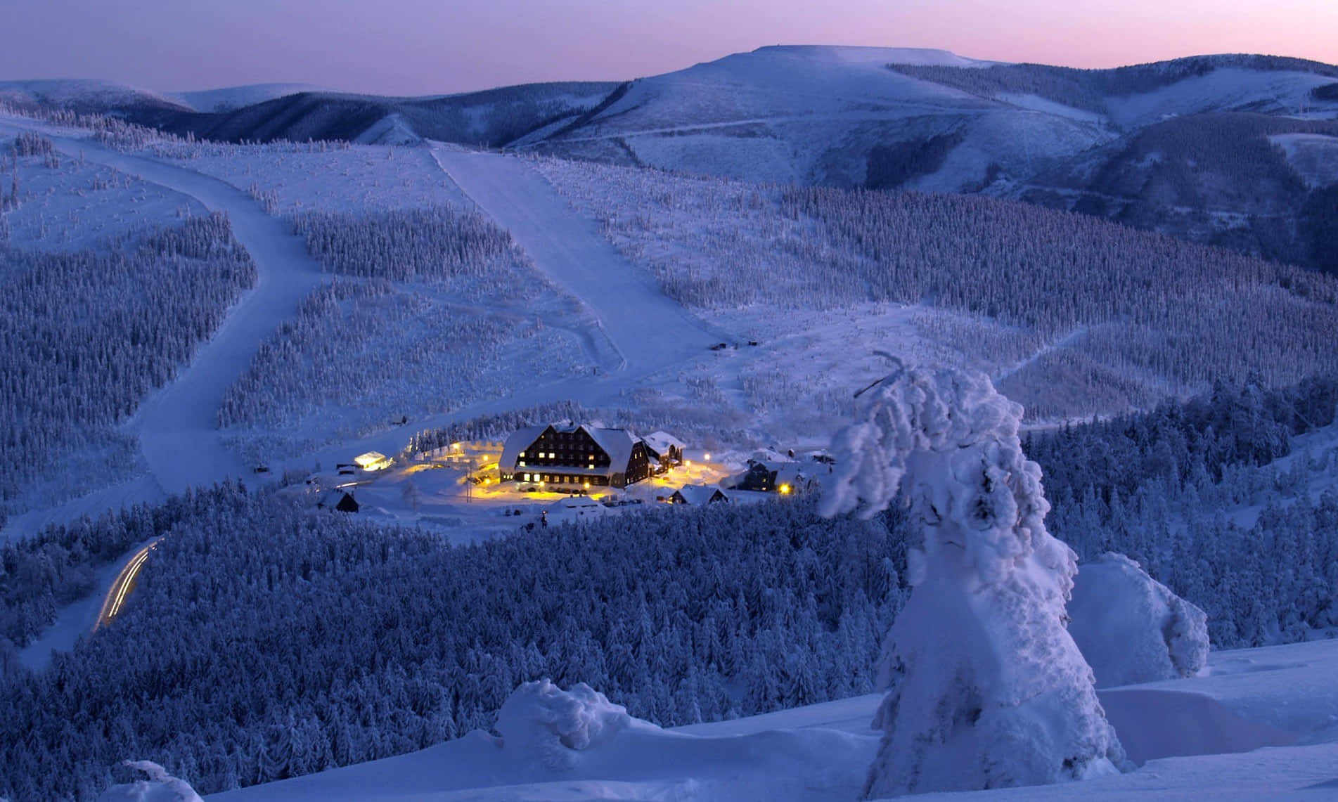 積雪的山間小屋，溫暖燈光在暮色中閃耀。