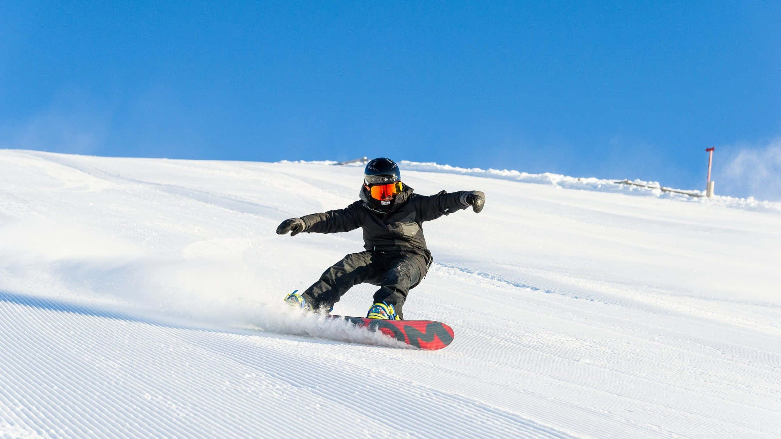 Winter Sports 桌布 壁紙 — 滑雪板手在清澈的藍天下，在經過修整的雪地上刻劃，留下一道粉雪痕跡。