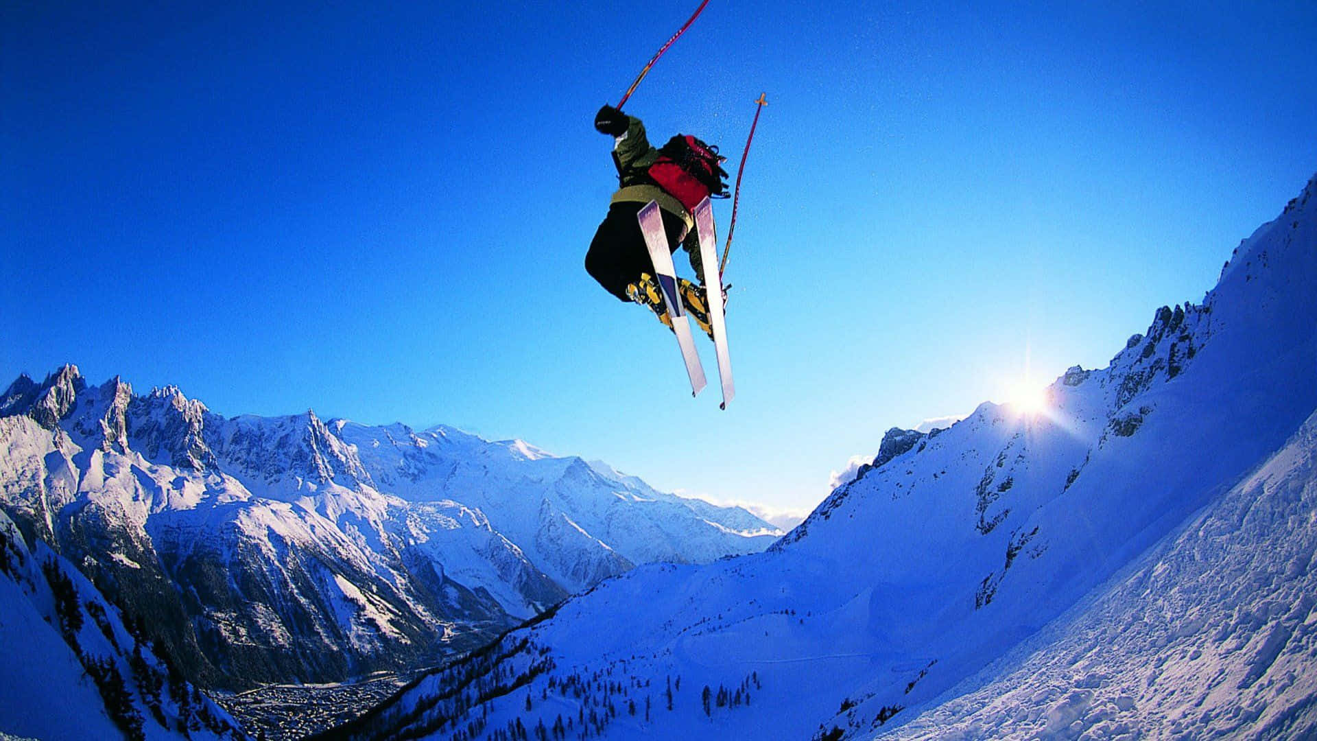 Skiing 桌布 壁紙 — 滑雪運動員在白雪覆蓋的山峰之上，穿過清澈的藍天，伴隨著耀眼的陽光。