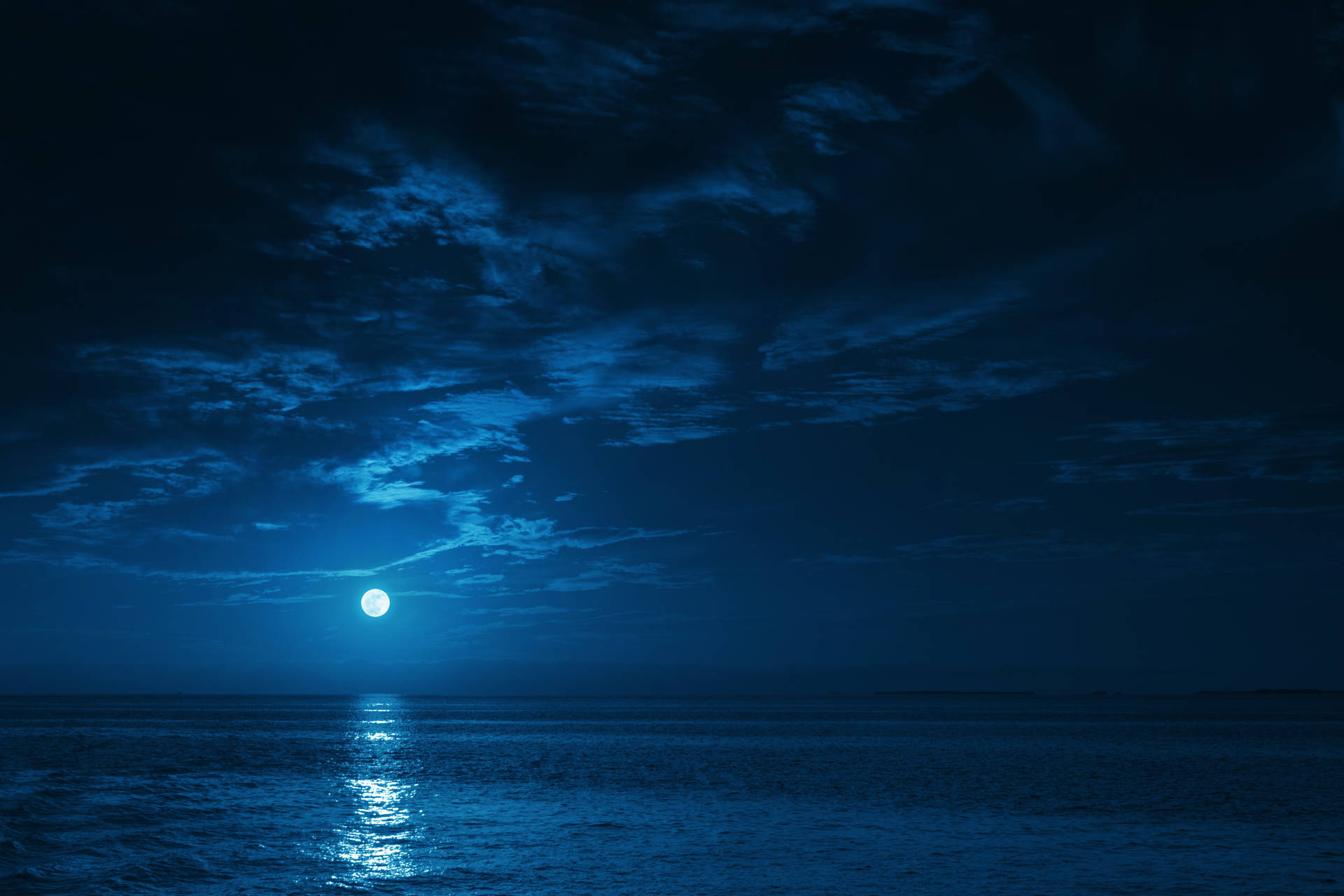 滿月在多雲的夜空下照耀著平靜的海水。