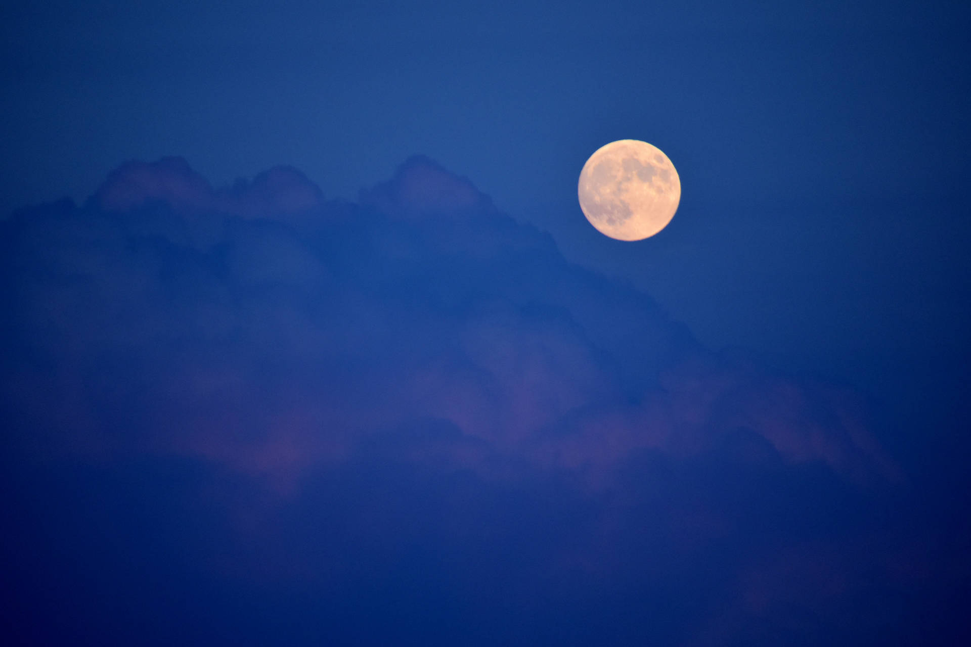 滿月在深藍色夜空中從紫色雲層後升起。
