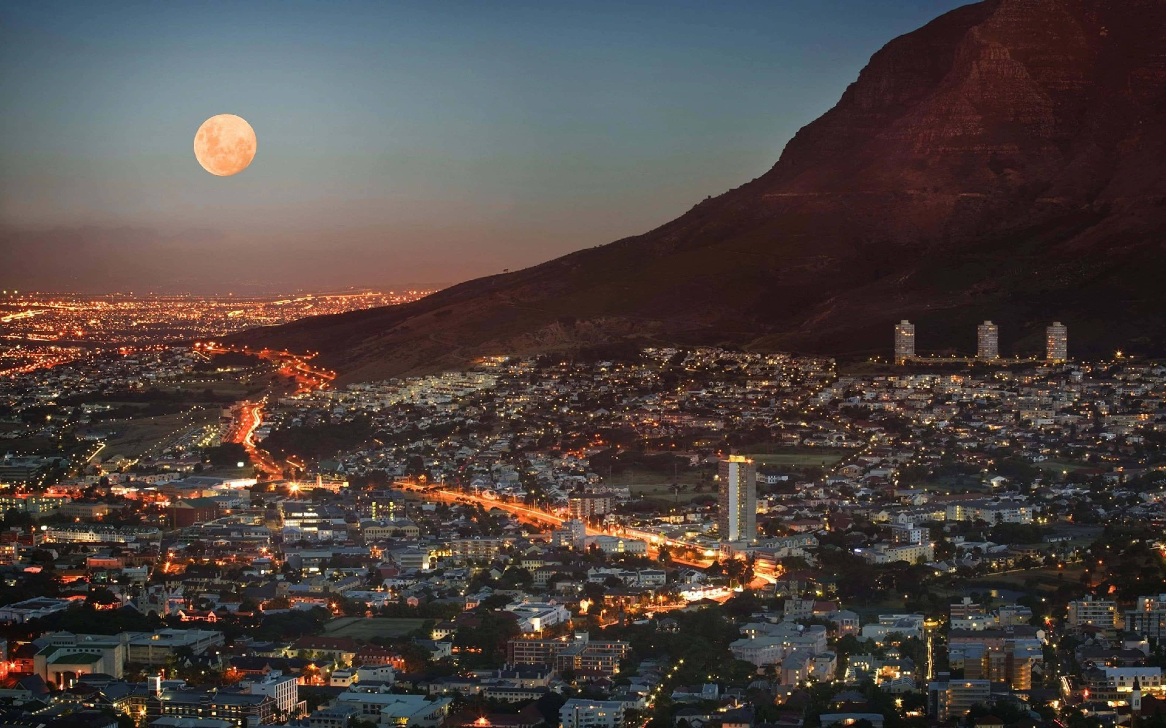 South Africa 桌布 壁紙 — 滿月升起於暮色中依偎著巨大山脈的廣闊城市景觀之上。