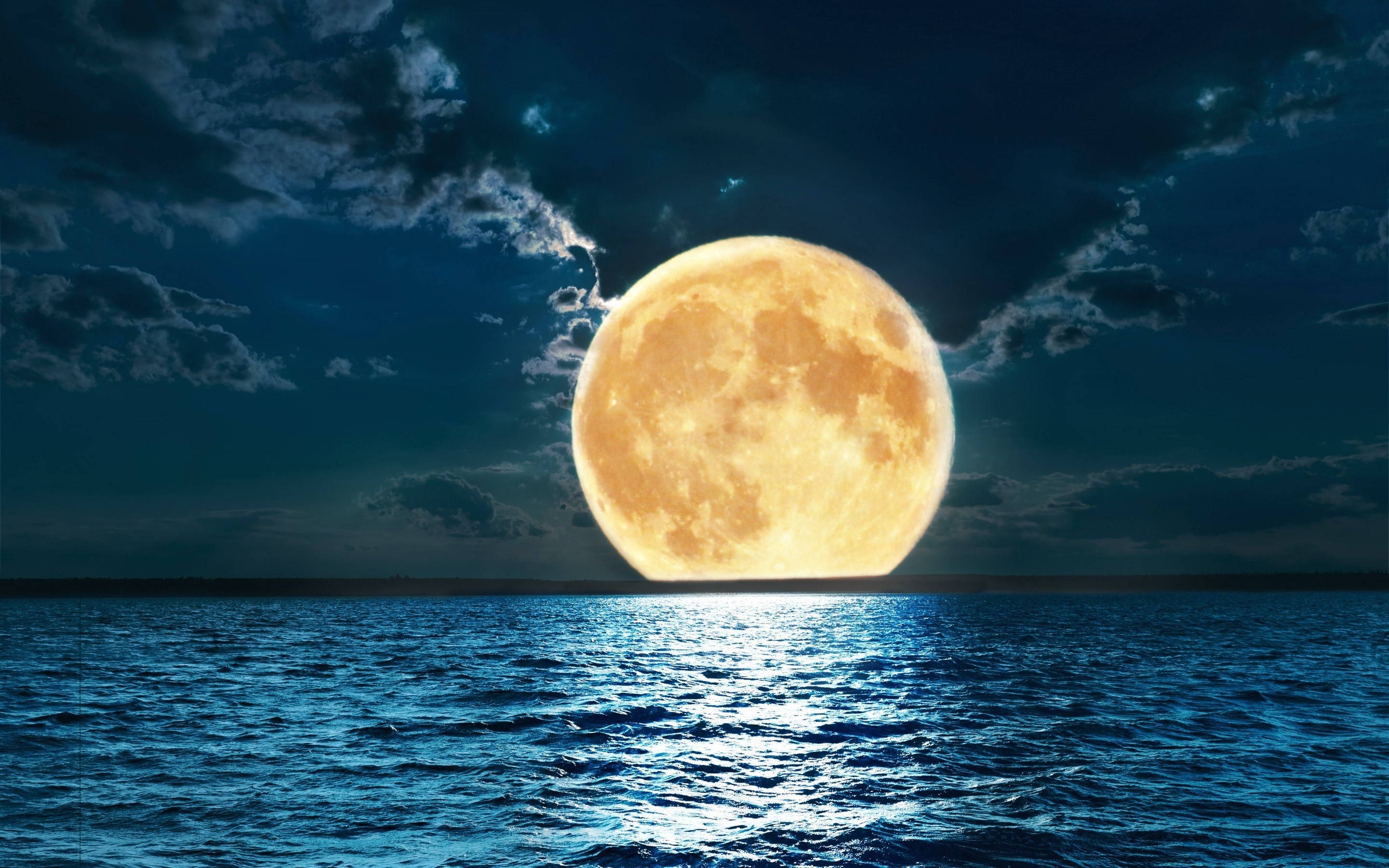 滿月灑落寧靜海洋 壁紙 — 一顆巨大的發光滿月在多雲的夜空下從深藍色的海洋上升起。