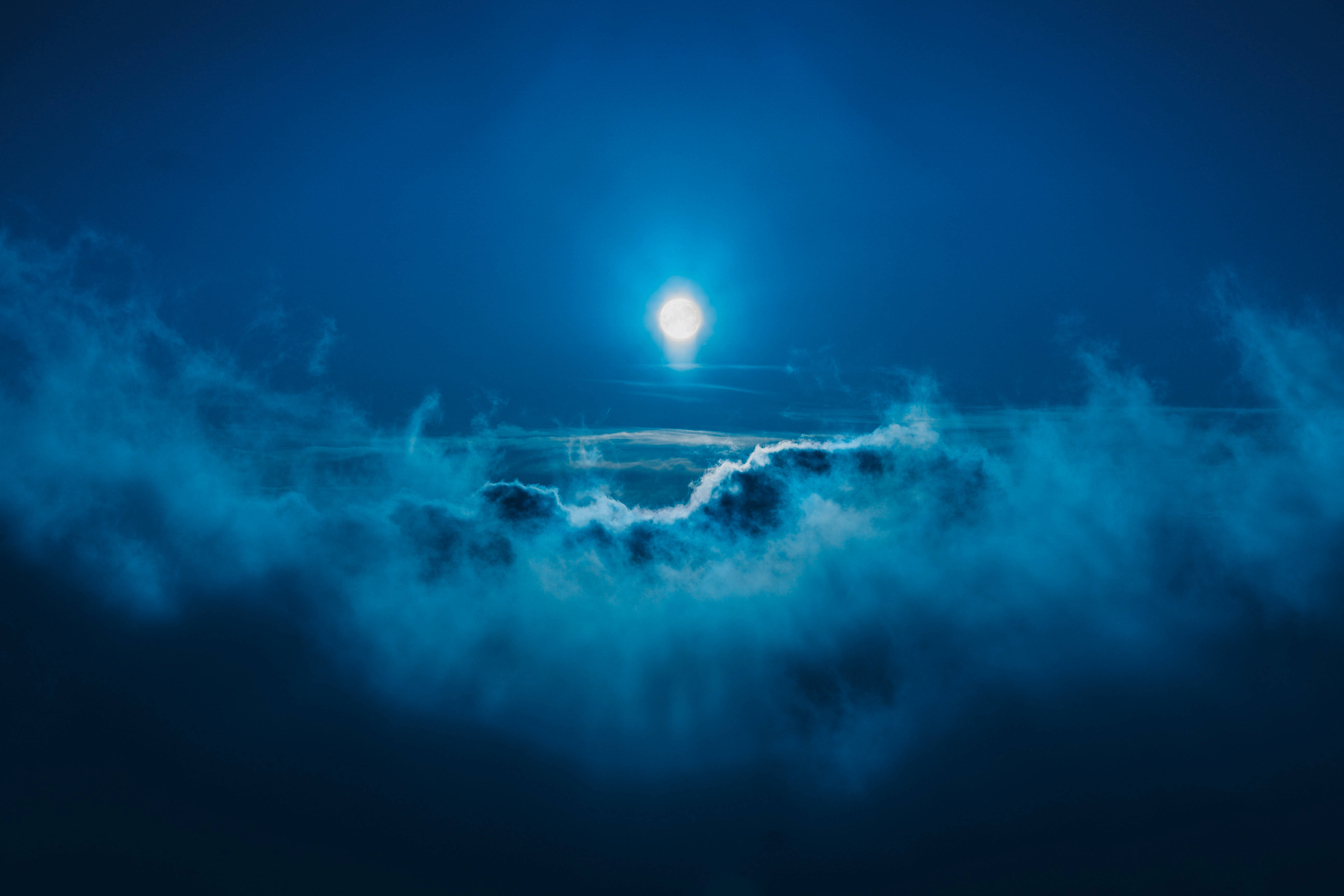 滿月穿過深藍雲層 壁紙 — 一輪明亮的滿月穿過旋轉的藍色雲層，在深邃的夜空中發光。